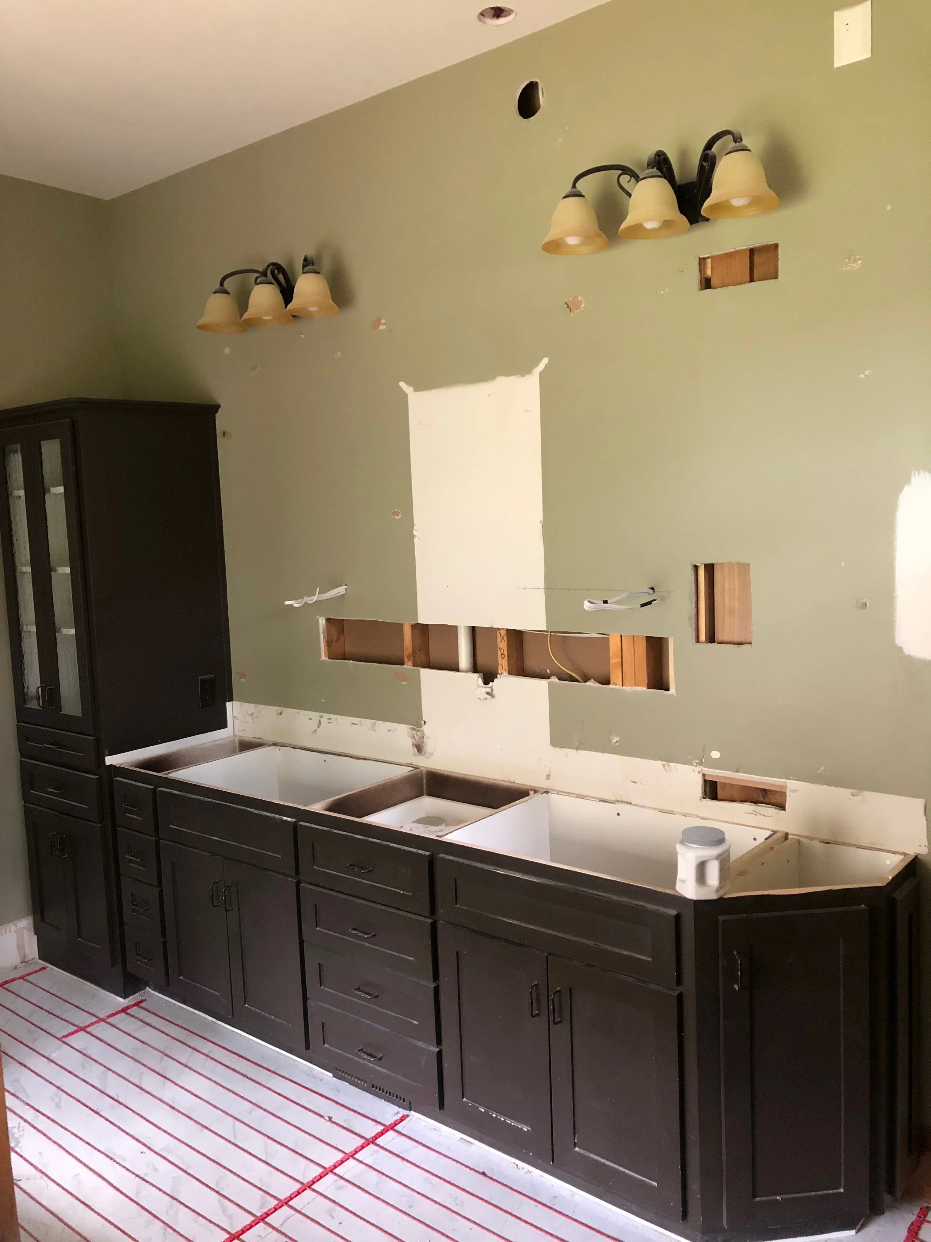 Bathroom vanity with black cabinetry, sage green walls, dual sink openings, and wall-mounted light fixtures