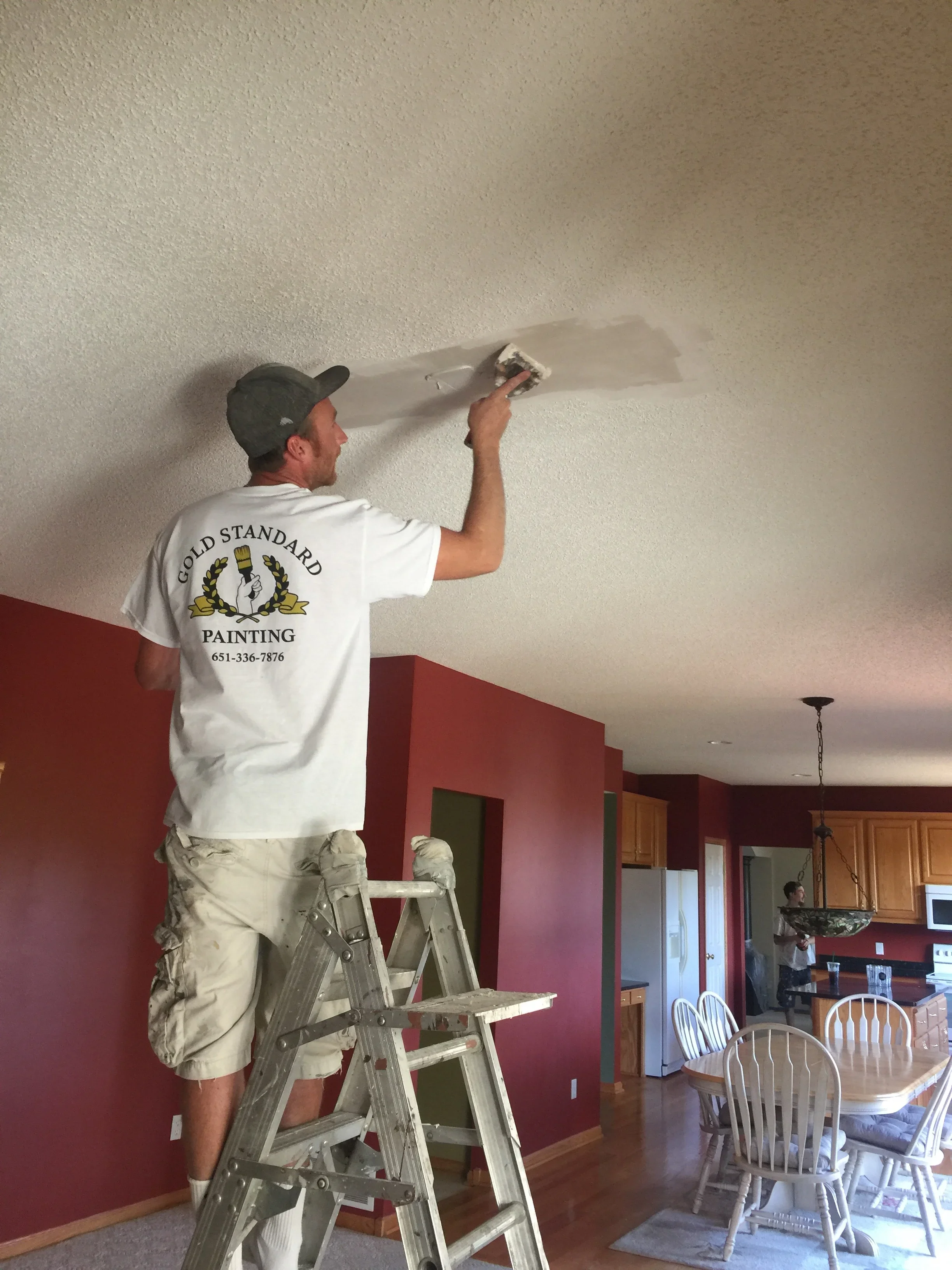 Painter on ladder applying joint compound to drywall ceiling seams