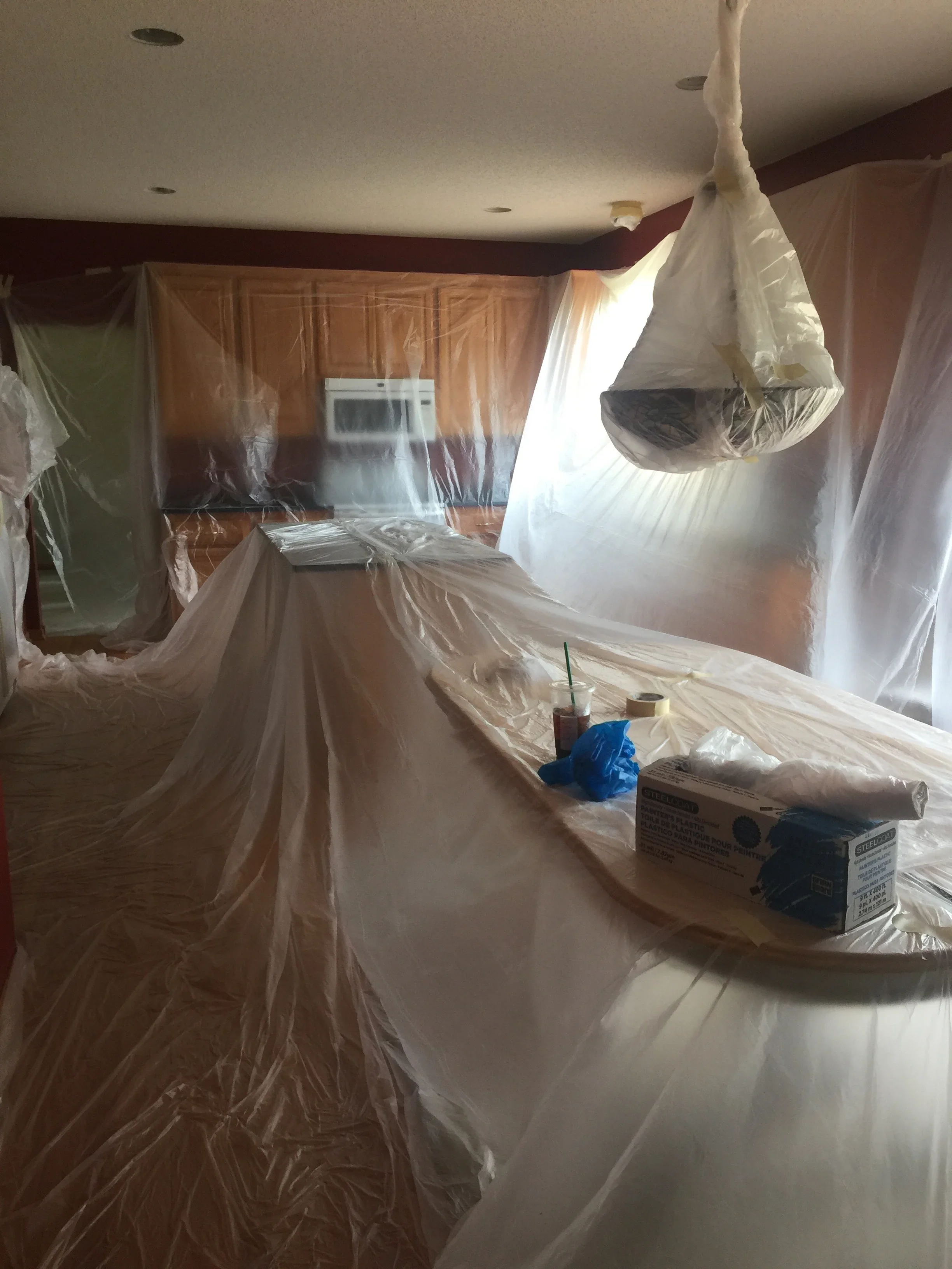 Kitchen interior with plastic sheeting protecting cabinets, appliances, and surfaces during painting preparation