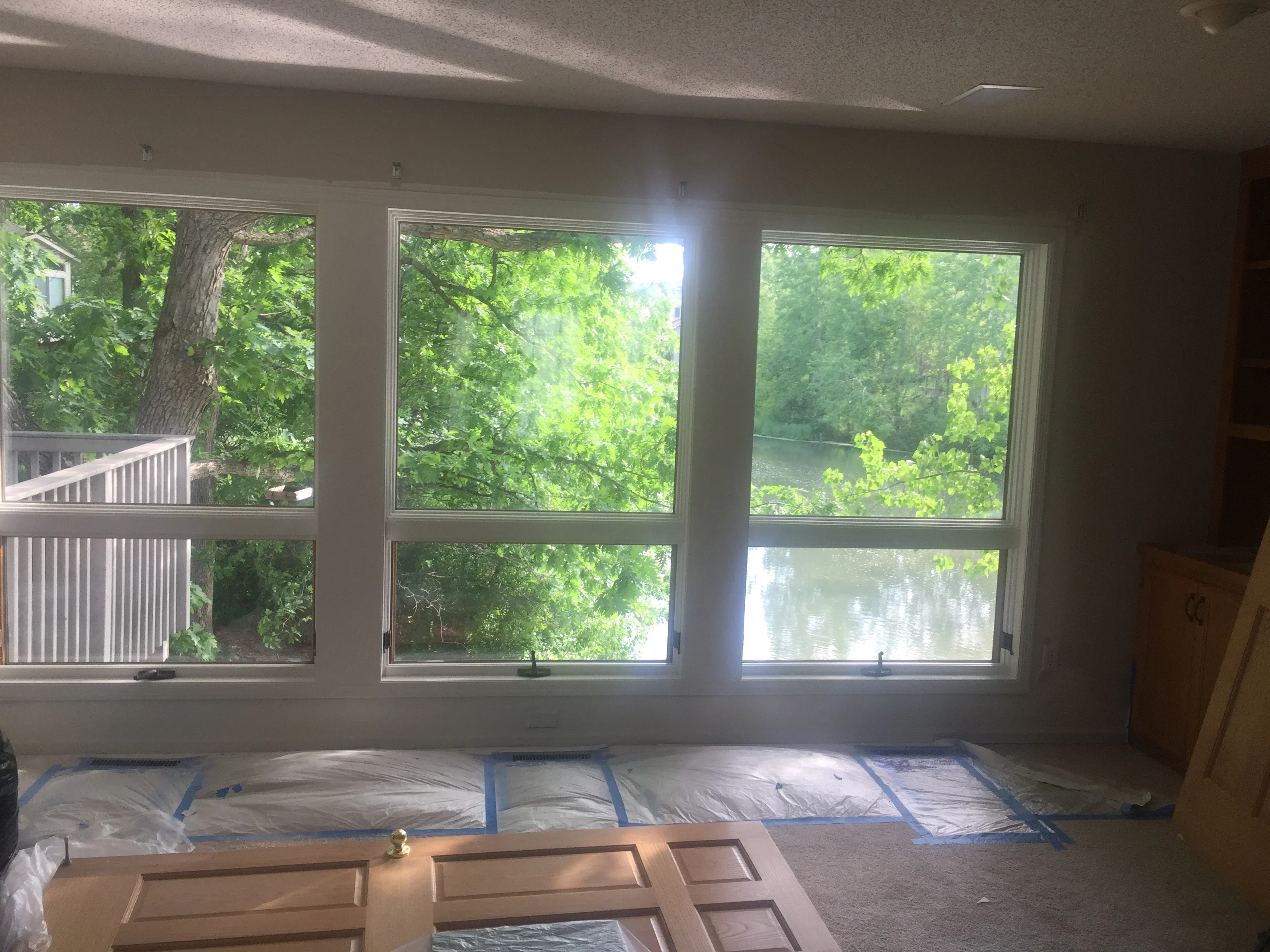 Interior room with white-painted walls and ceiling, three large casement windows overlooking trees and water