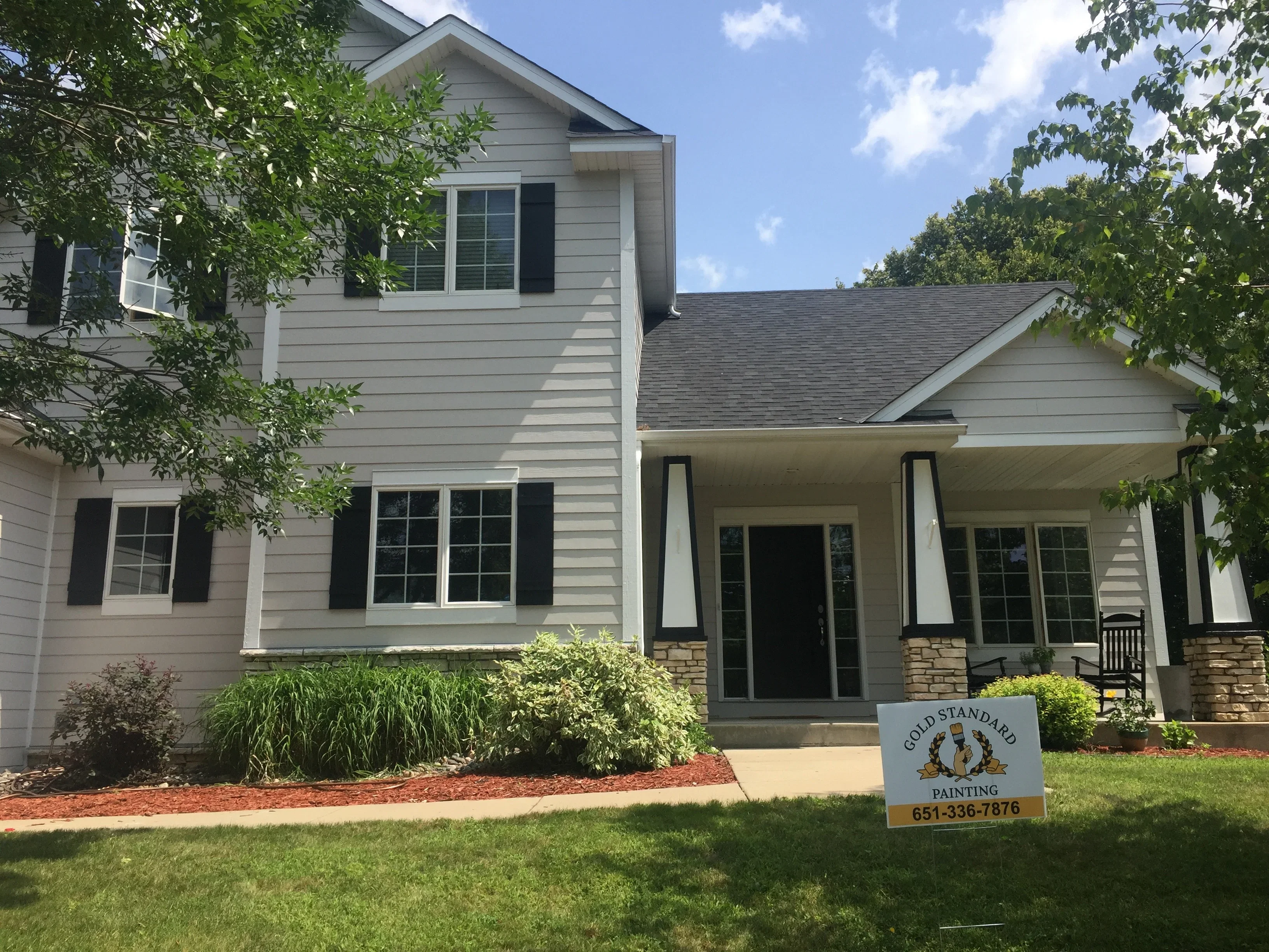 Two-story house with gray siding, white trim, black shutters, and painted front porch columns