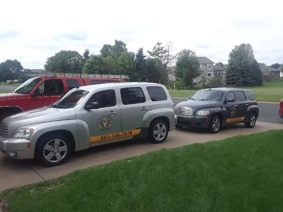 Two service vehicles with custom painted wraps, logos, and lettering on driveway