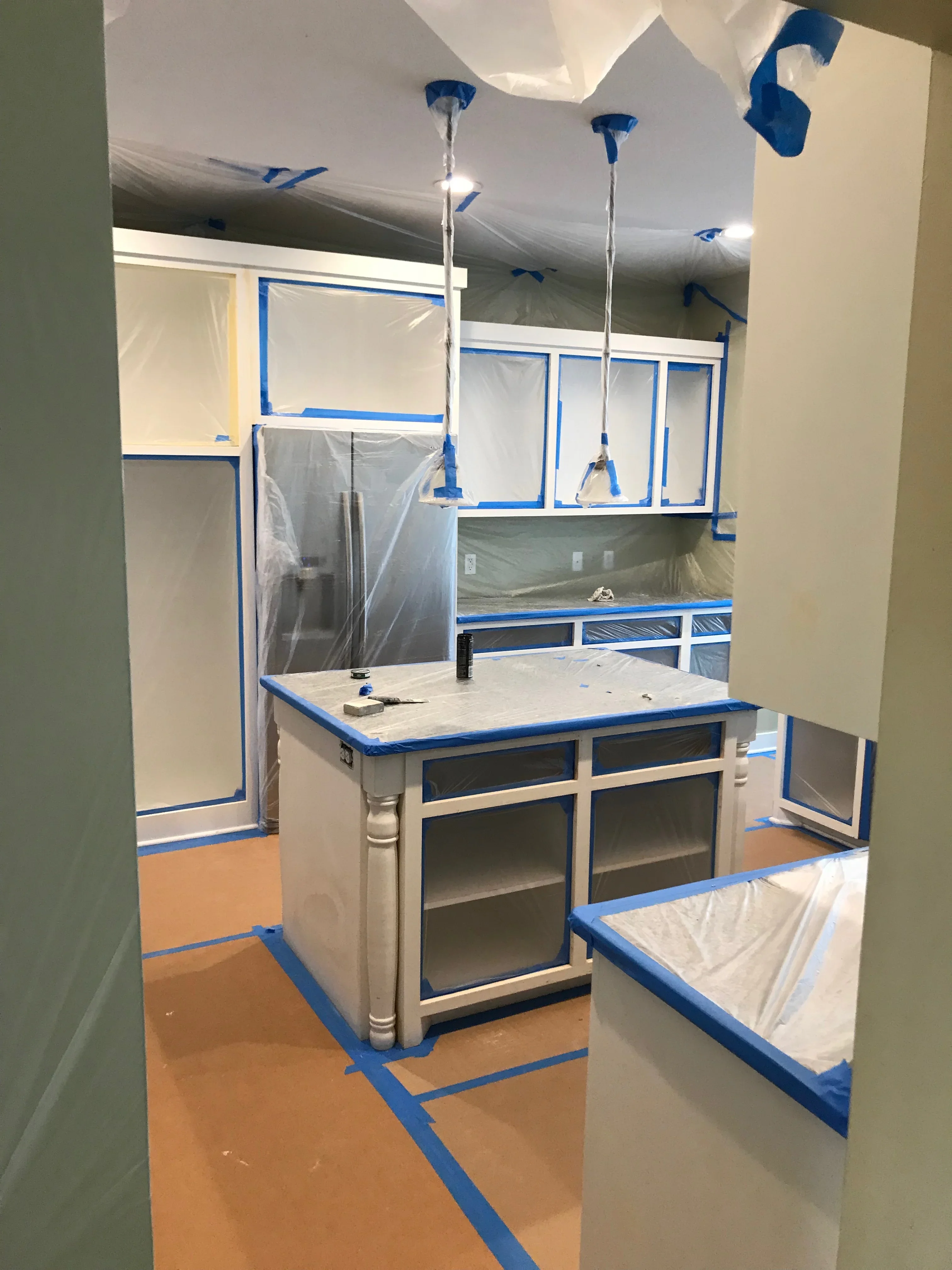 Kitchen interior with blue painter's tape, plastic sheeting, custom cabinetry, and protected surfaces during renovation