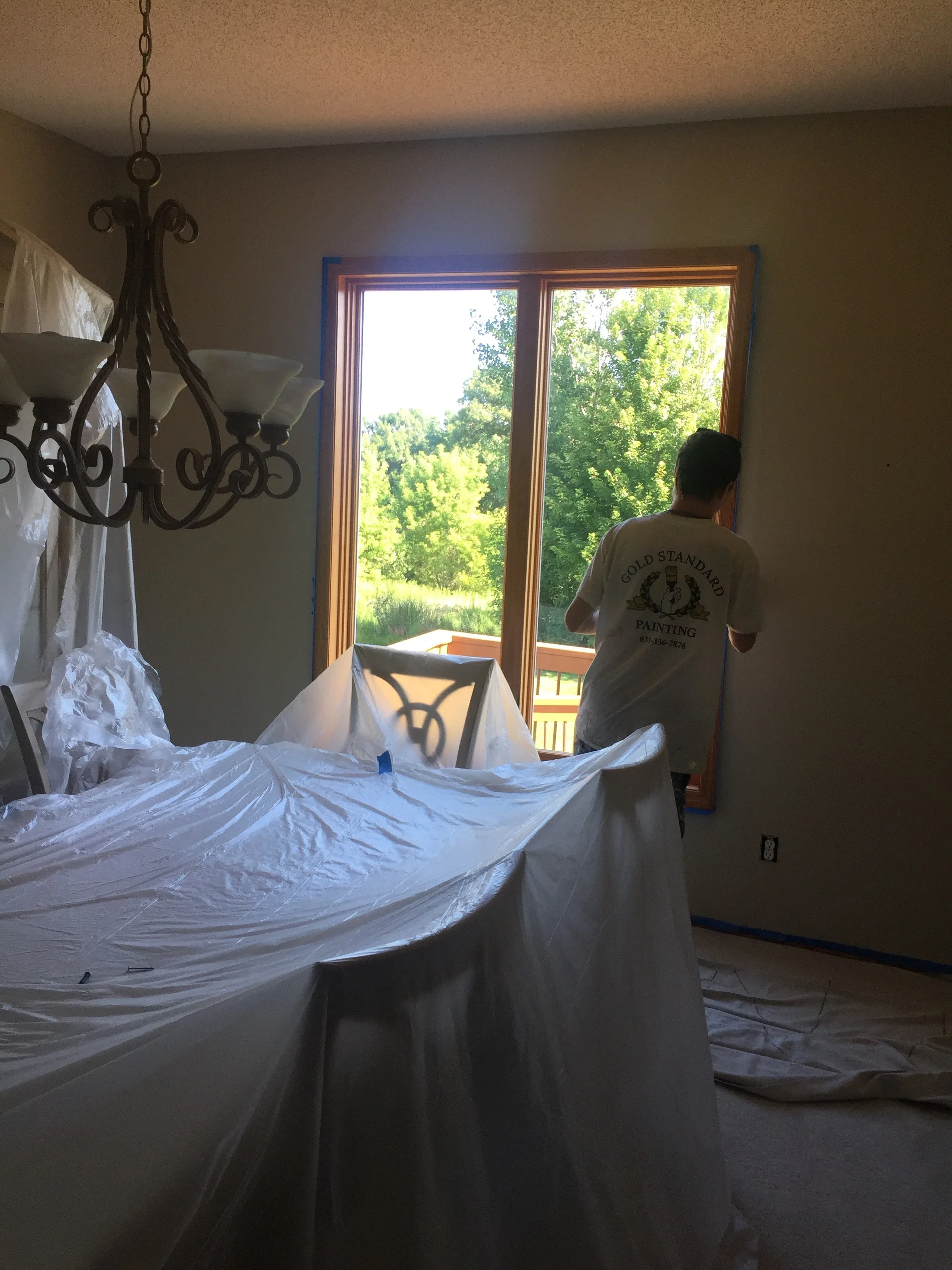 Interior room with plastic sheeting protecting furniture, painter working near French doors with wood trim