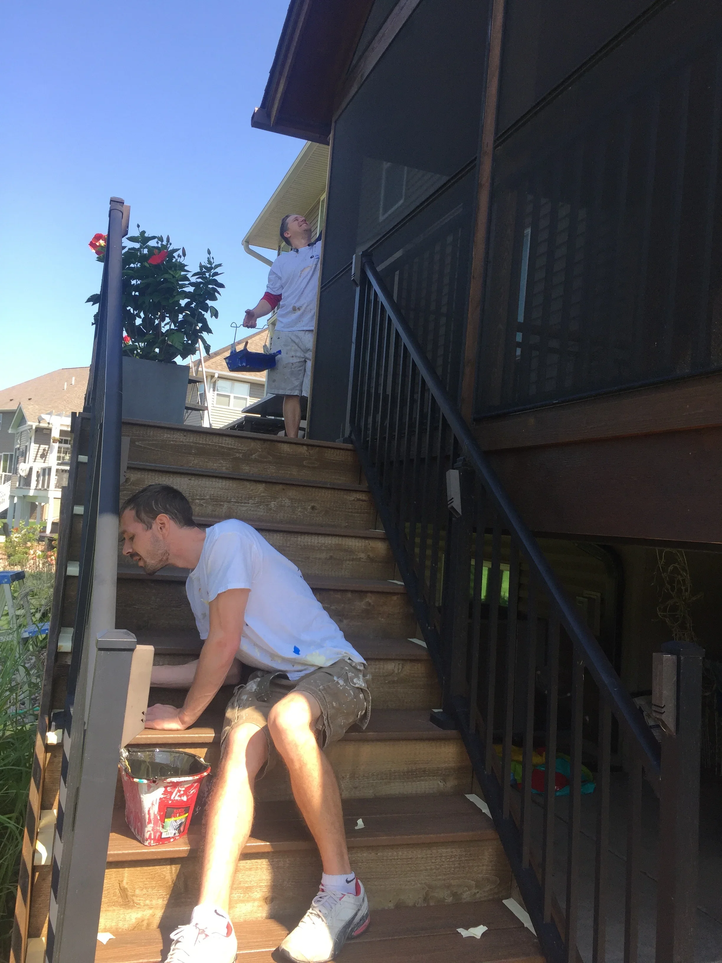 Workers staining wooden deck stairs and railings with protective finish