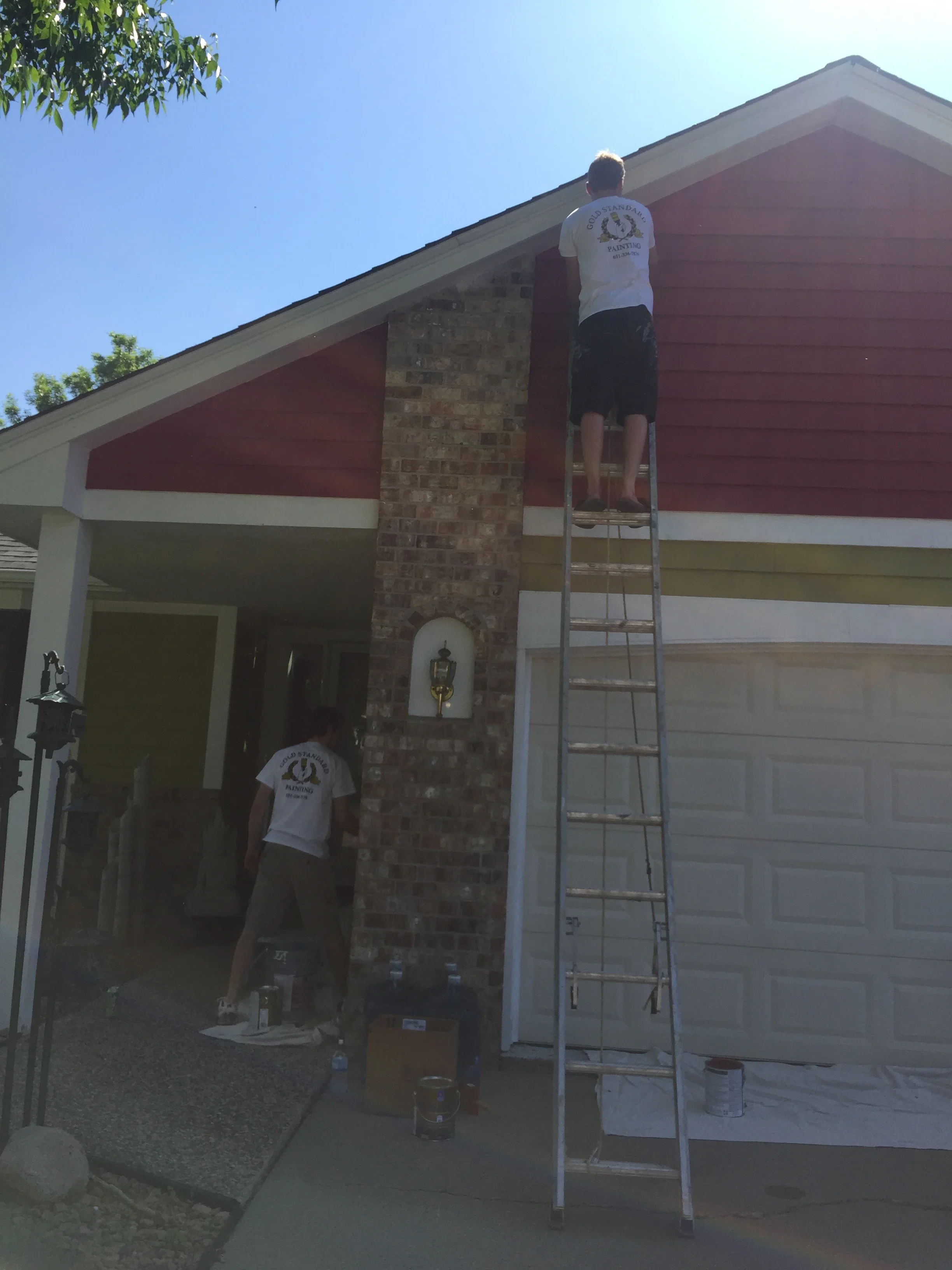 Painters on ladders applying exterior paint to home with brick chimney and horizontal trim bands