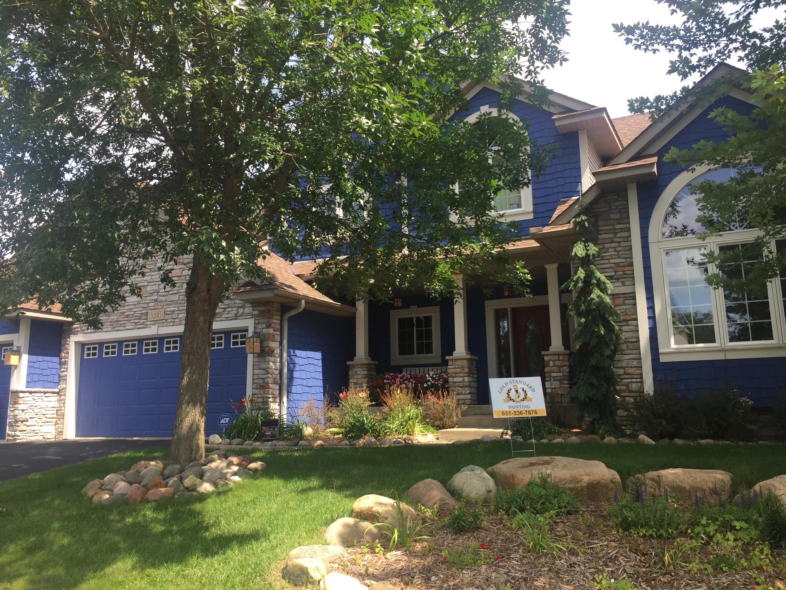 Blue exterior house paint with stone foundation, blue garage doors, and white trim on two-story home