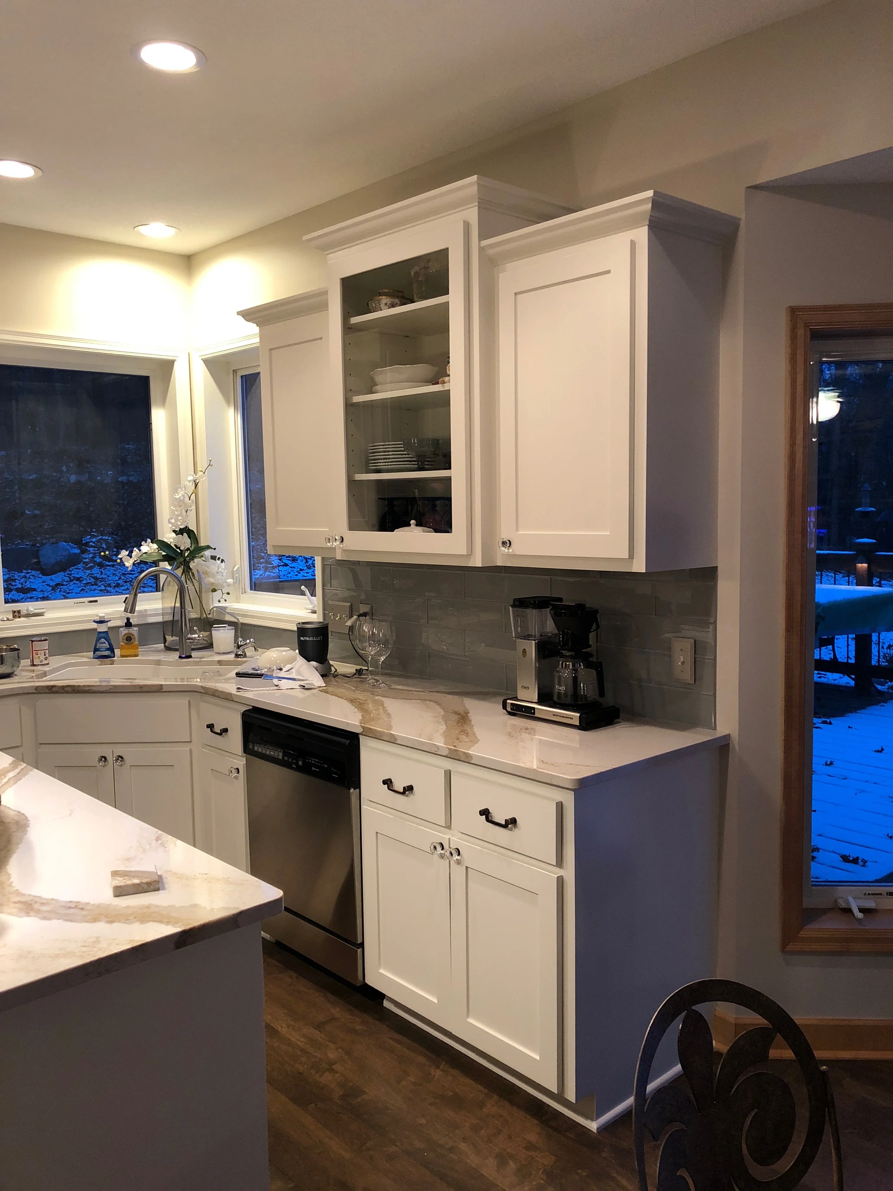 White painted kitchen cabinets with shaker doors, gray tile backsplash, and neutral wall paint