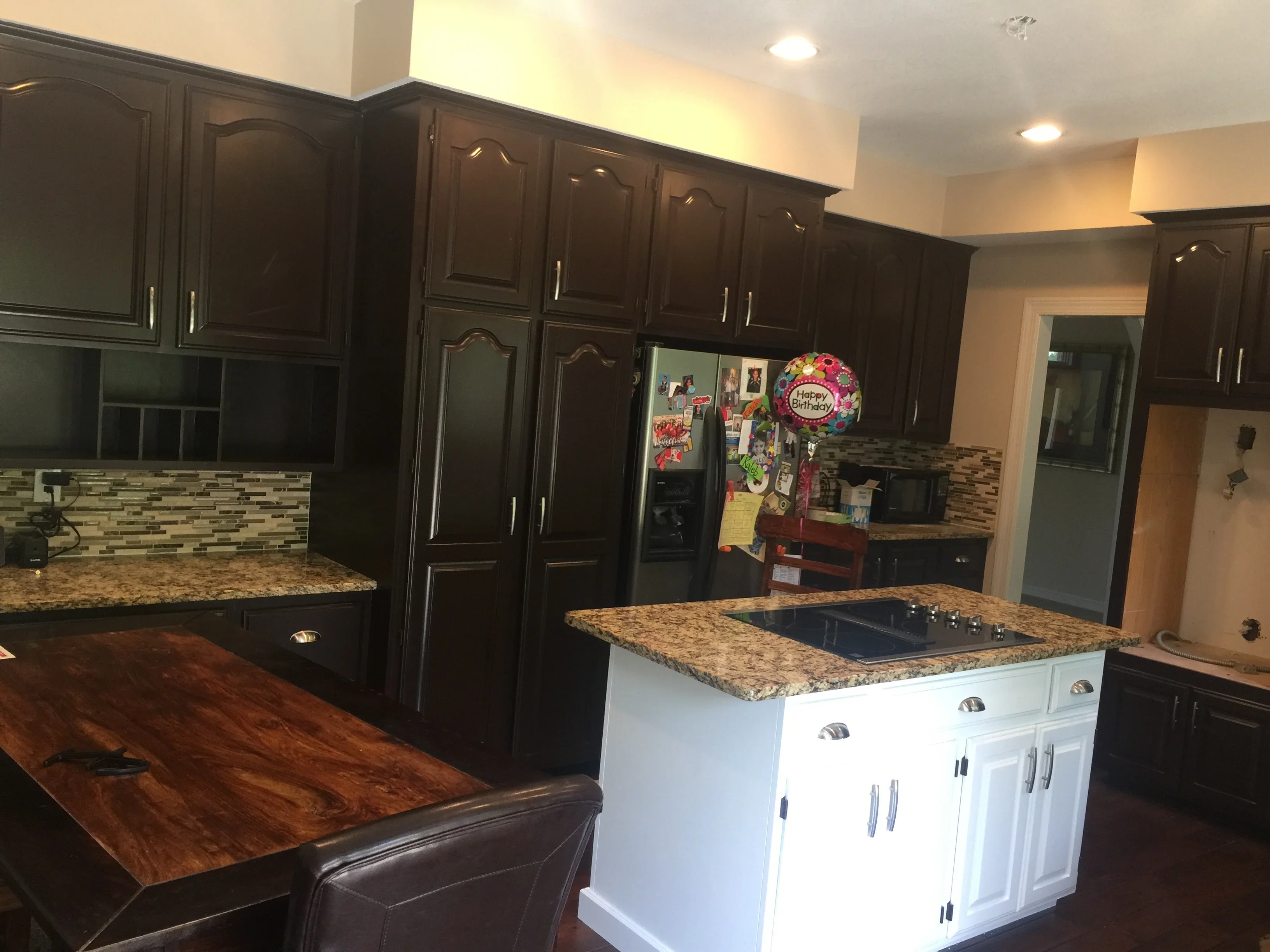 Dark espresso painted kitchen cabinets with white island base, granite counters, and mosaic tile backsplash
