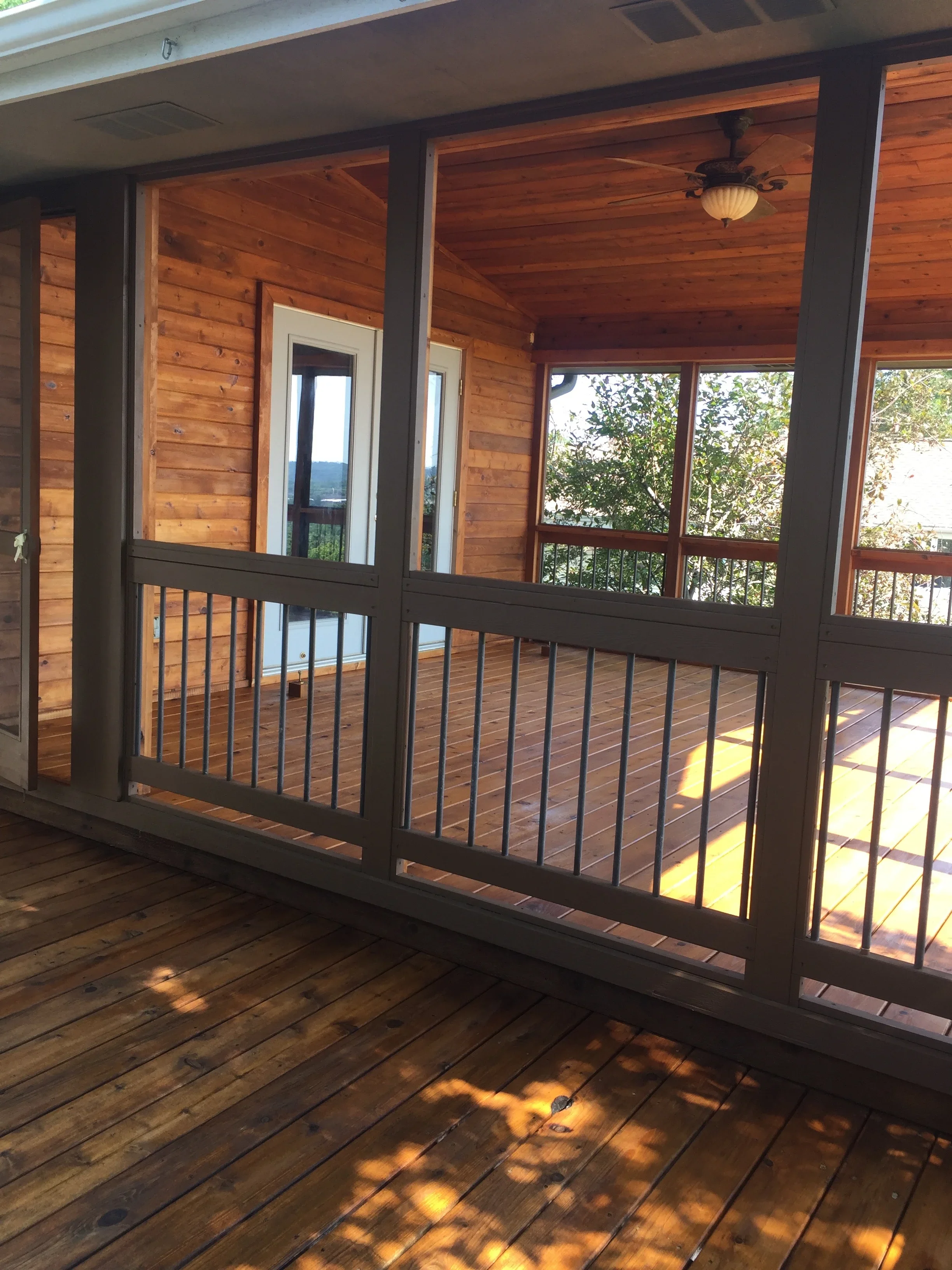 Screened porch interior with cedar wood ceiling, dark stained railings, and white-trimmed doors