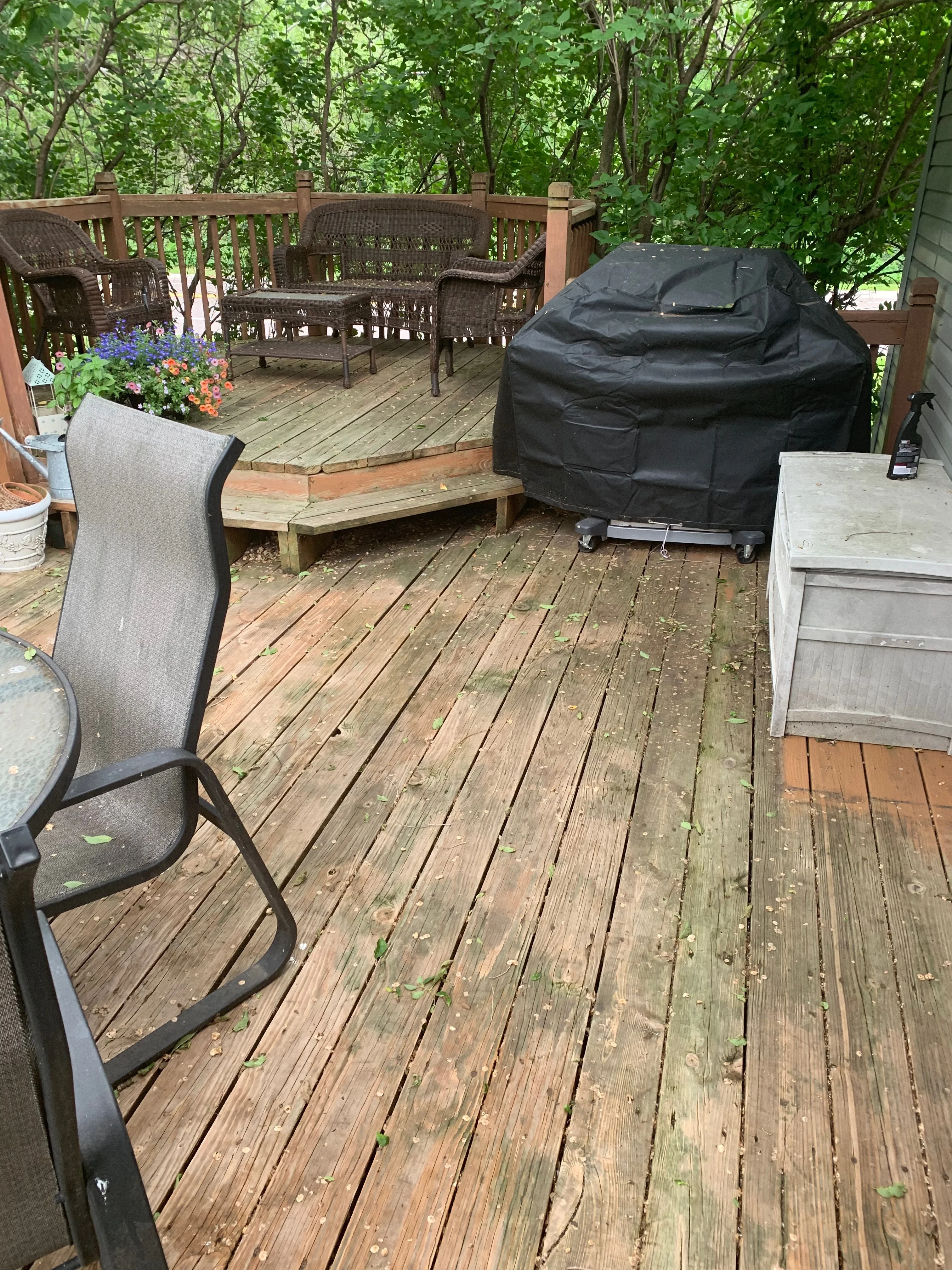 Wooden deck with railings, wicker furniture, and protective covering on grill