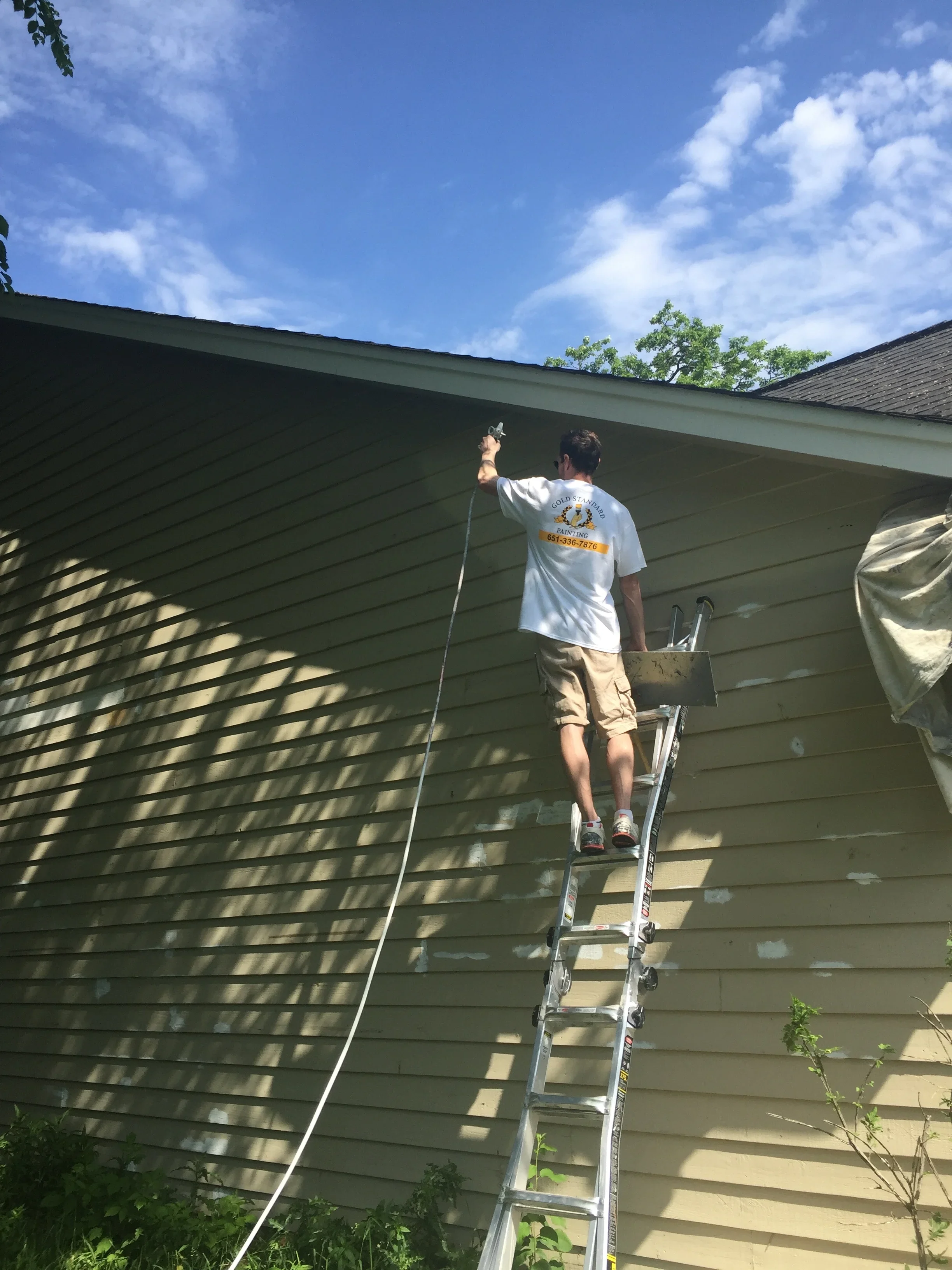 Painter on ladder applying exterior paint to vinyl siding with horizontal board pattern