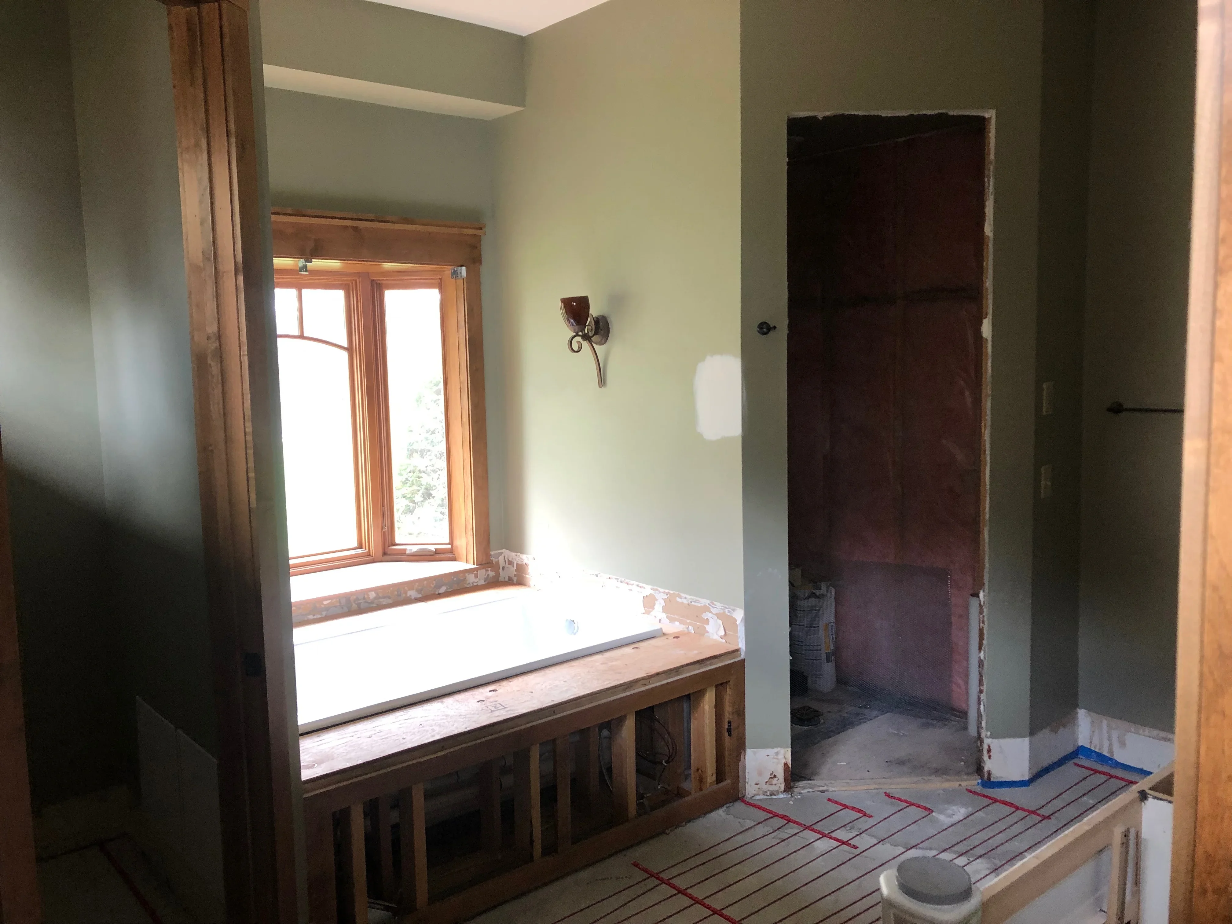 Sage green and cream painted bathroom walls with white trim, wood-framed window, and radiant floor heating lines