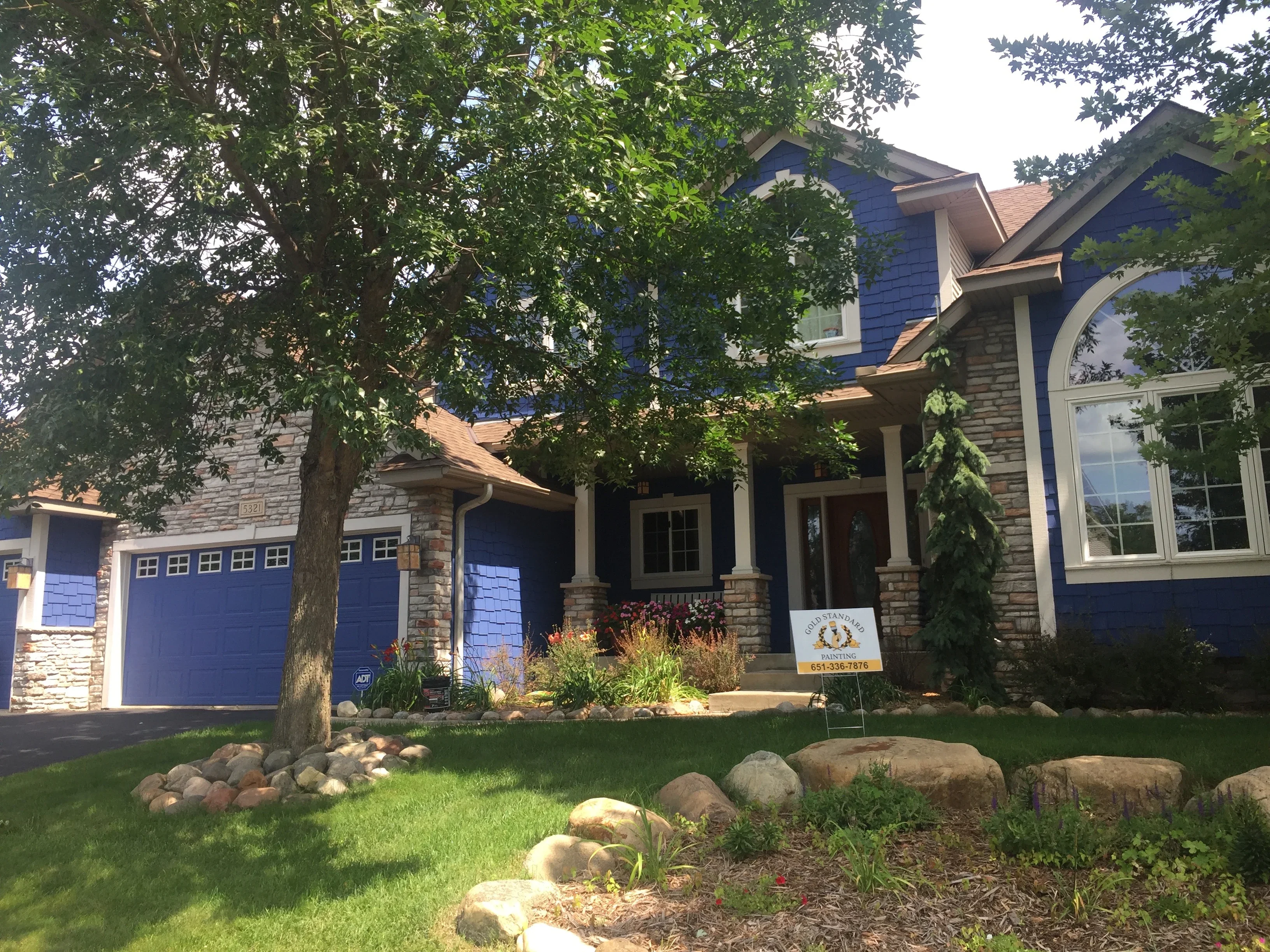 Blue and stone residential home with freshly painted exterior siding, trim, and garage doors