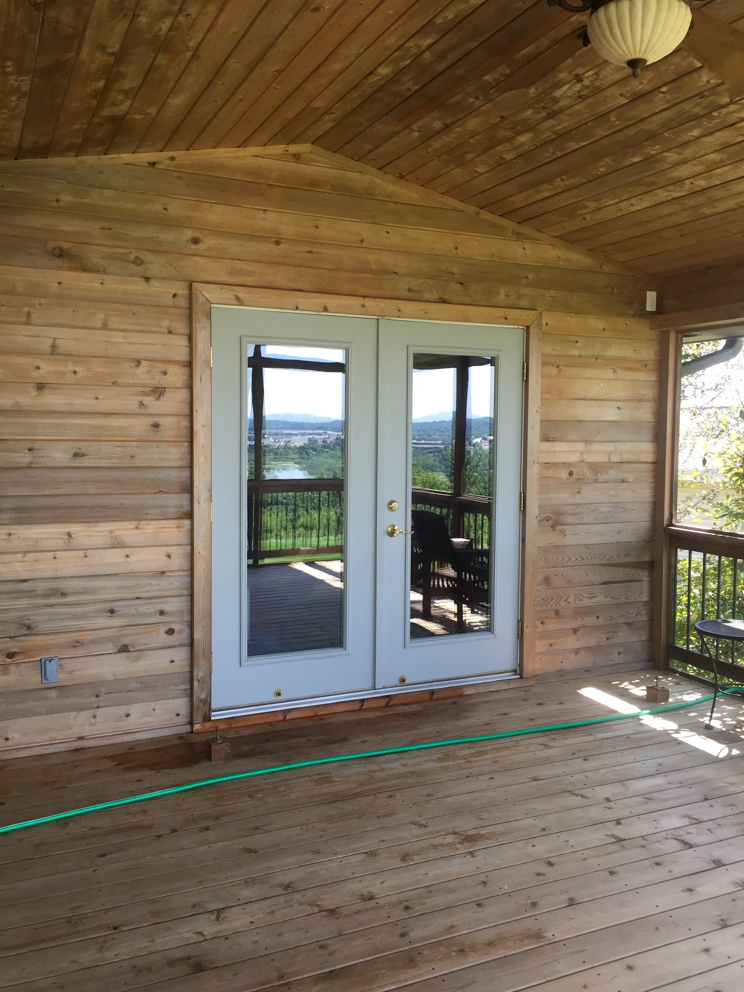 White-trimmed French doors with black frames in log cabin interior with wood plank walls and ceiling