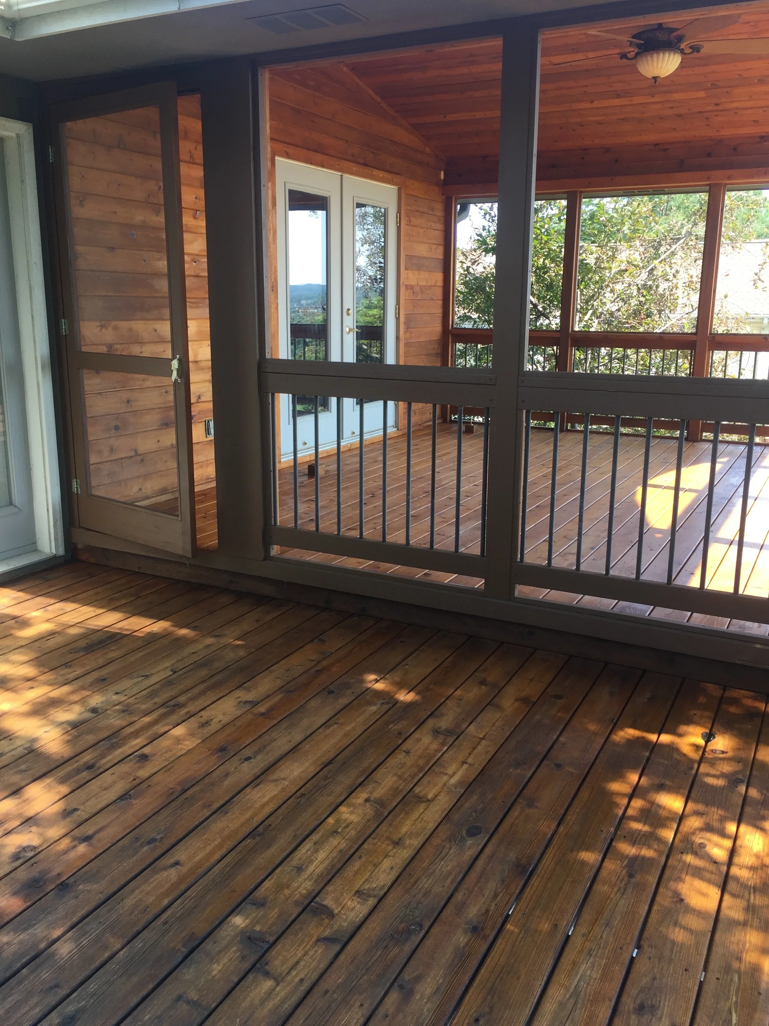 Stained wood deck and screened porch with dark frame, railing, and ceiling panels