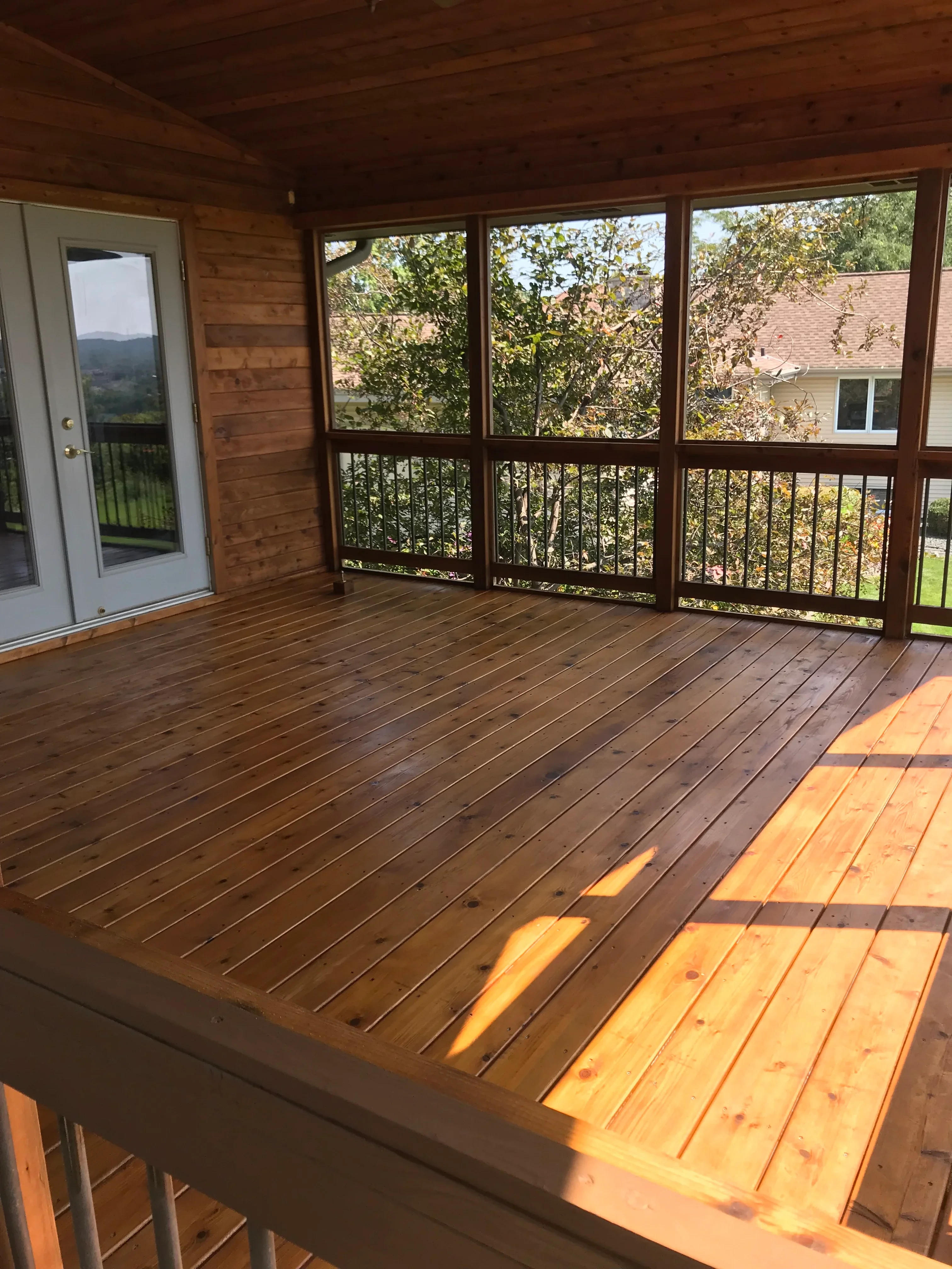 Screened deck with stained wood flooring, metal railings, and large window panels