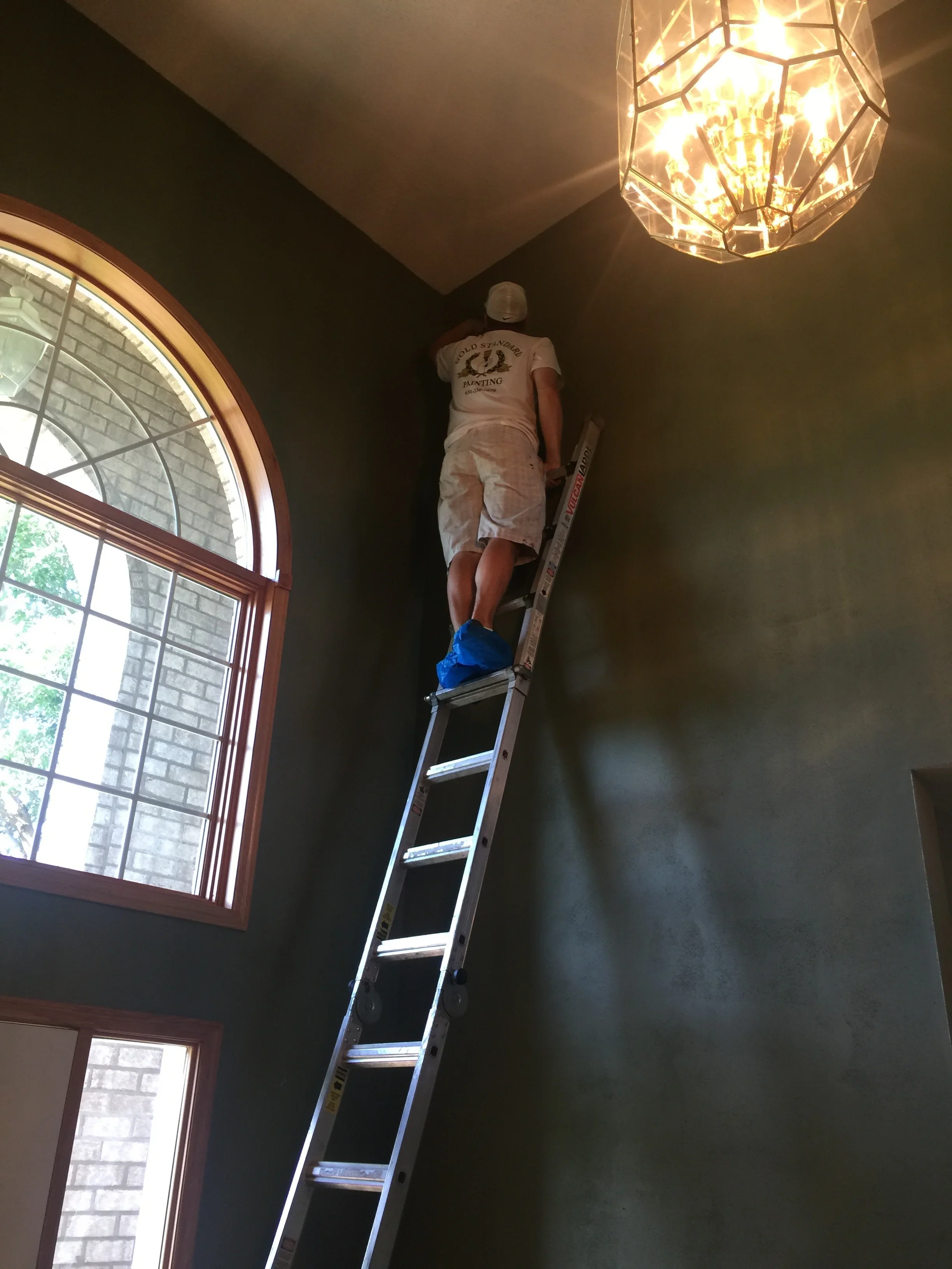 Painter on ladder installing pendant light fixture above dark painted walls and ceiling