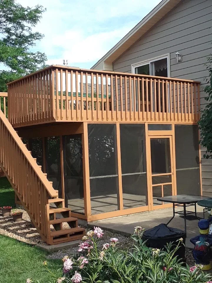 Elevated wooden deck with vertical railings and screened room enclosure with black screens and wood framing