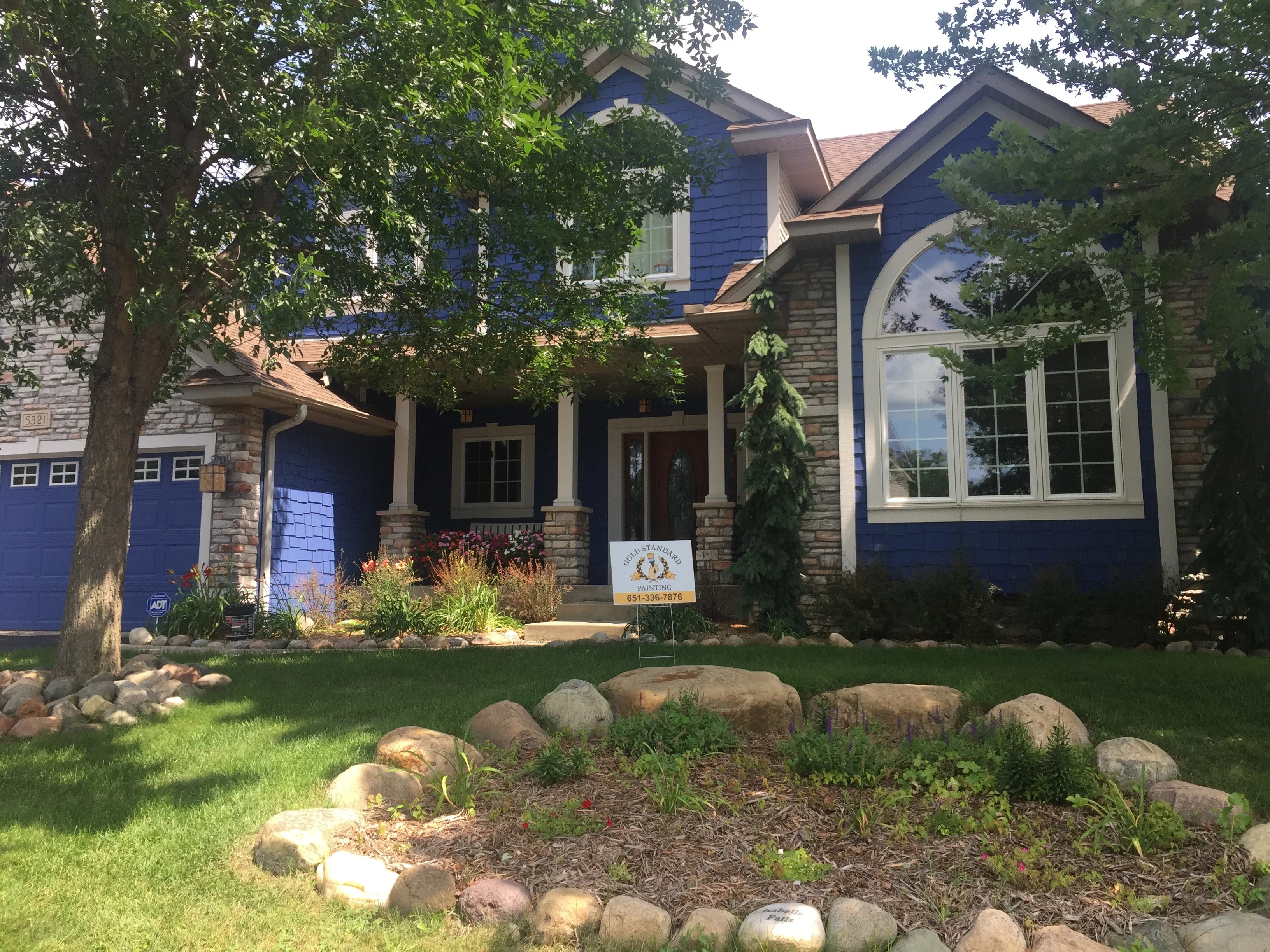 Two-story house with blue painted siding, stone foundation, white trim, and blue garage doors