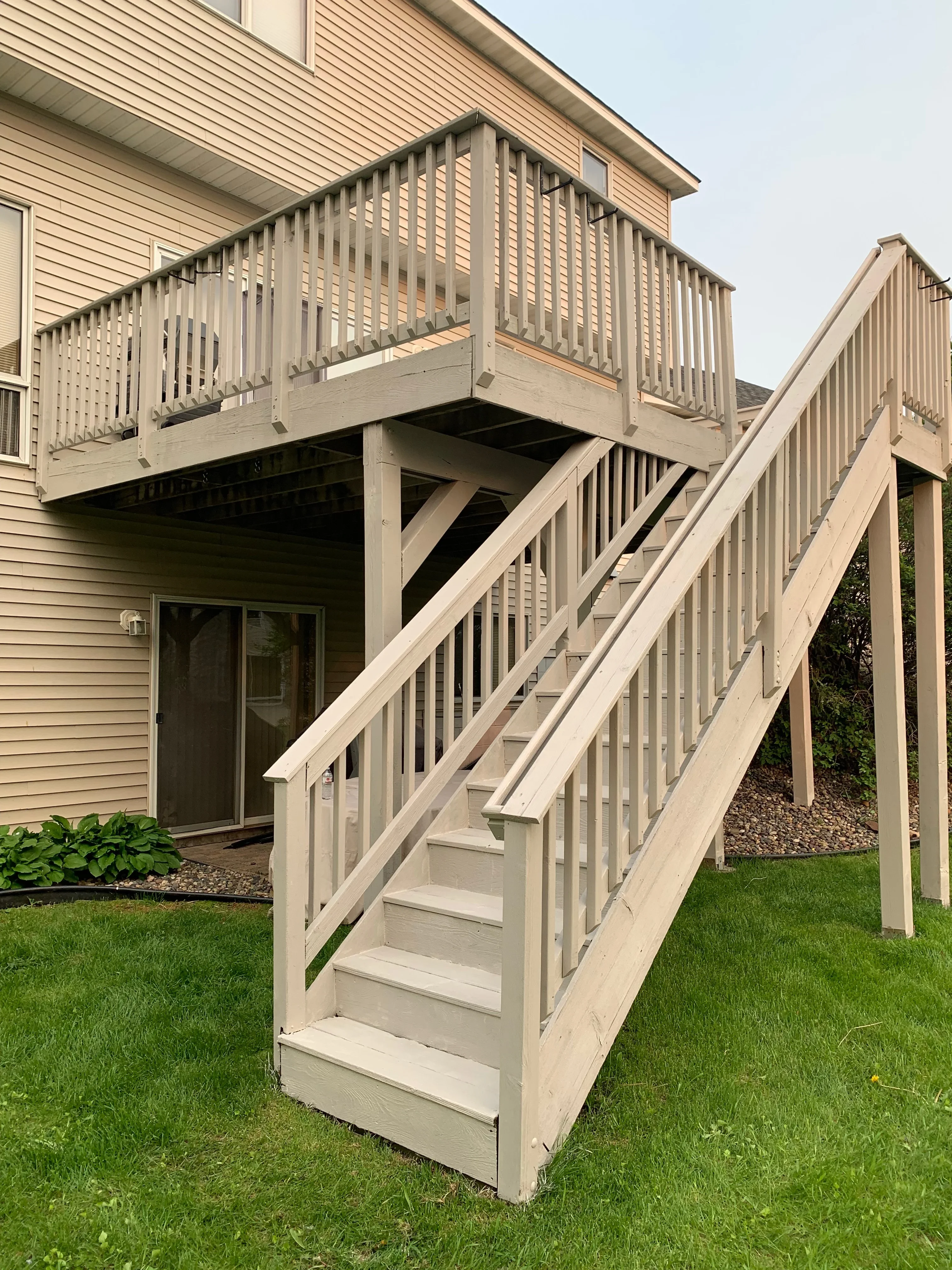 Two-story pressure-treated wood deck with vertical railings, exterior stairs, and support posts