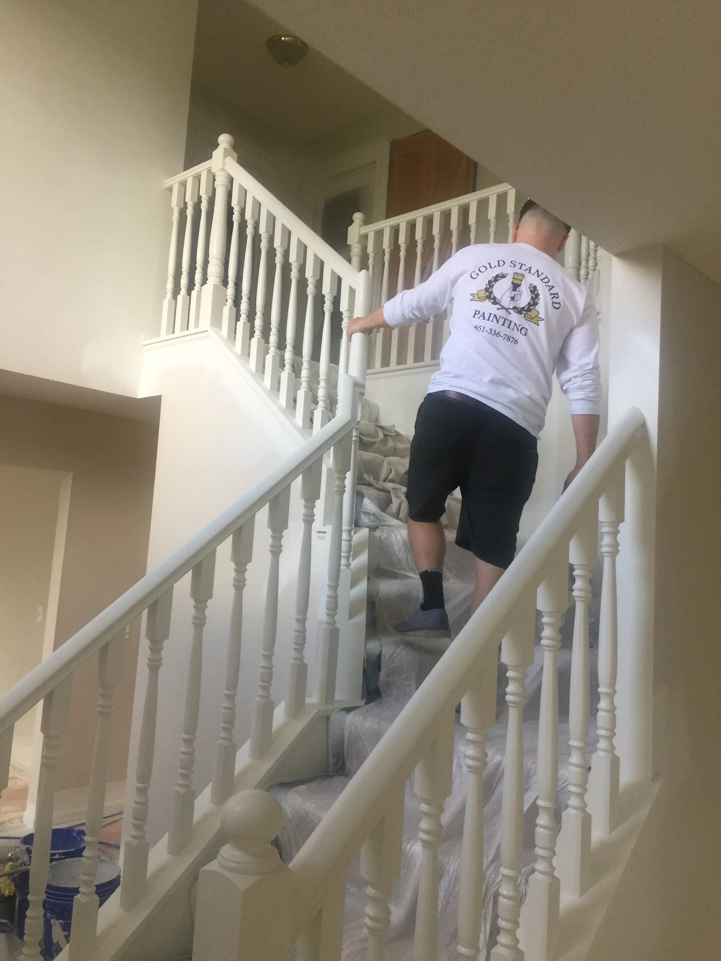 Painter applying white paint to interior staircase railings and balusters in residential home