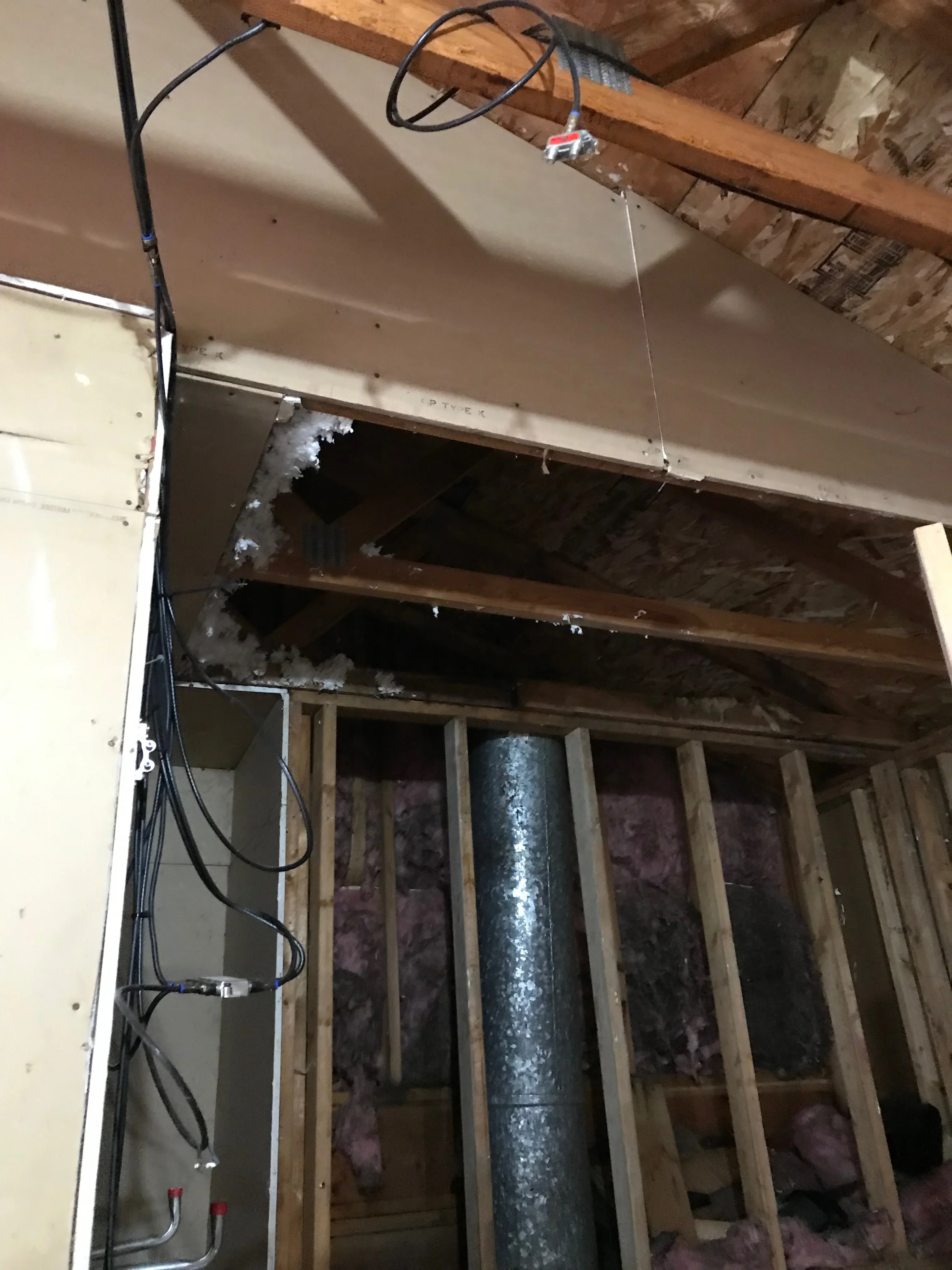 Drywall installation with wood framing, insulation, and electrical wiring in interior space