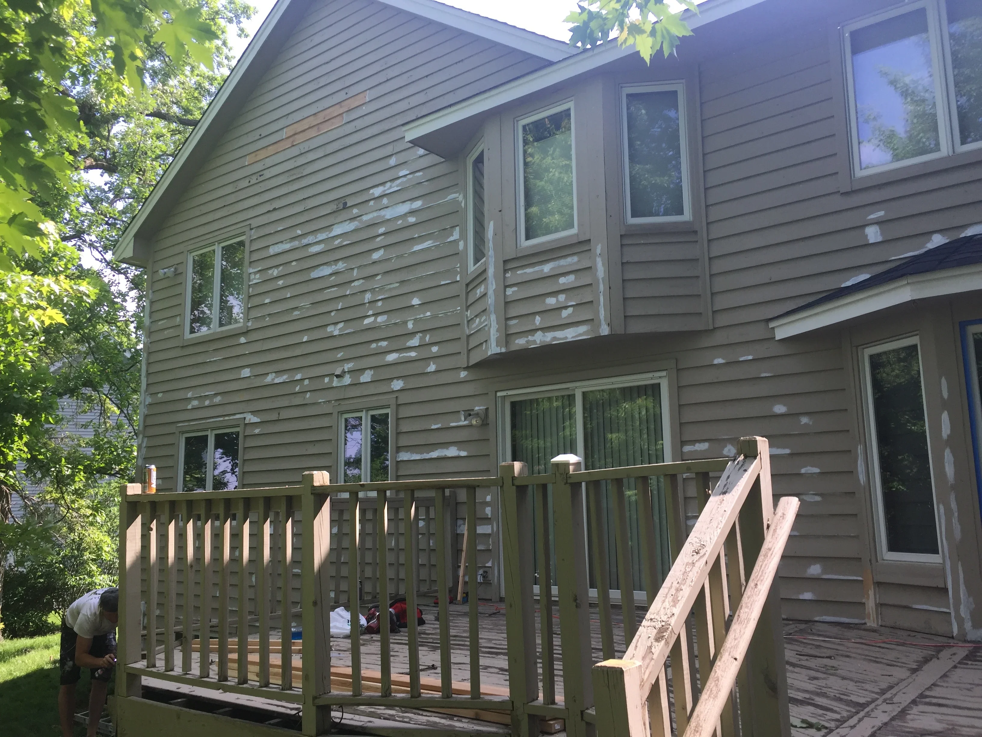 Two-story home with gray horizontal vinyl siding, multiple windows, and wooden deck with railing