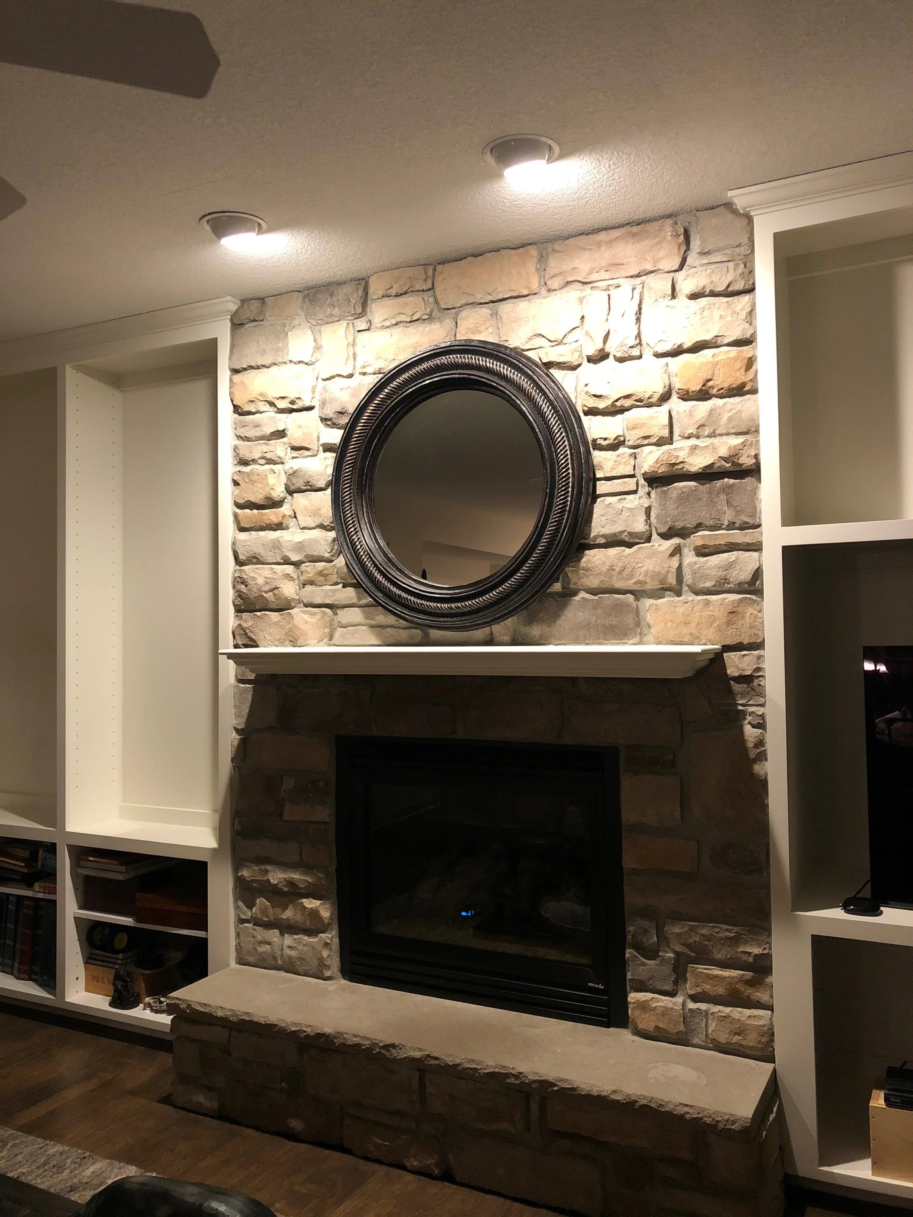 Stone fireplace with white painted built-in shelving, recessed lighting, and black electric insert