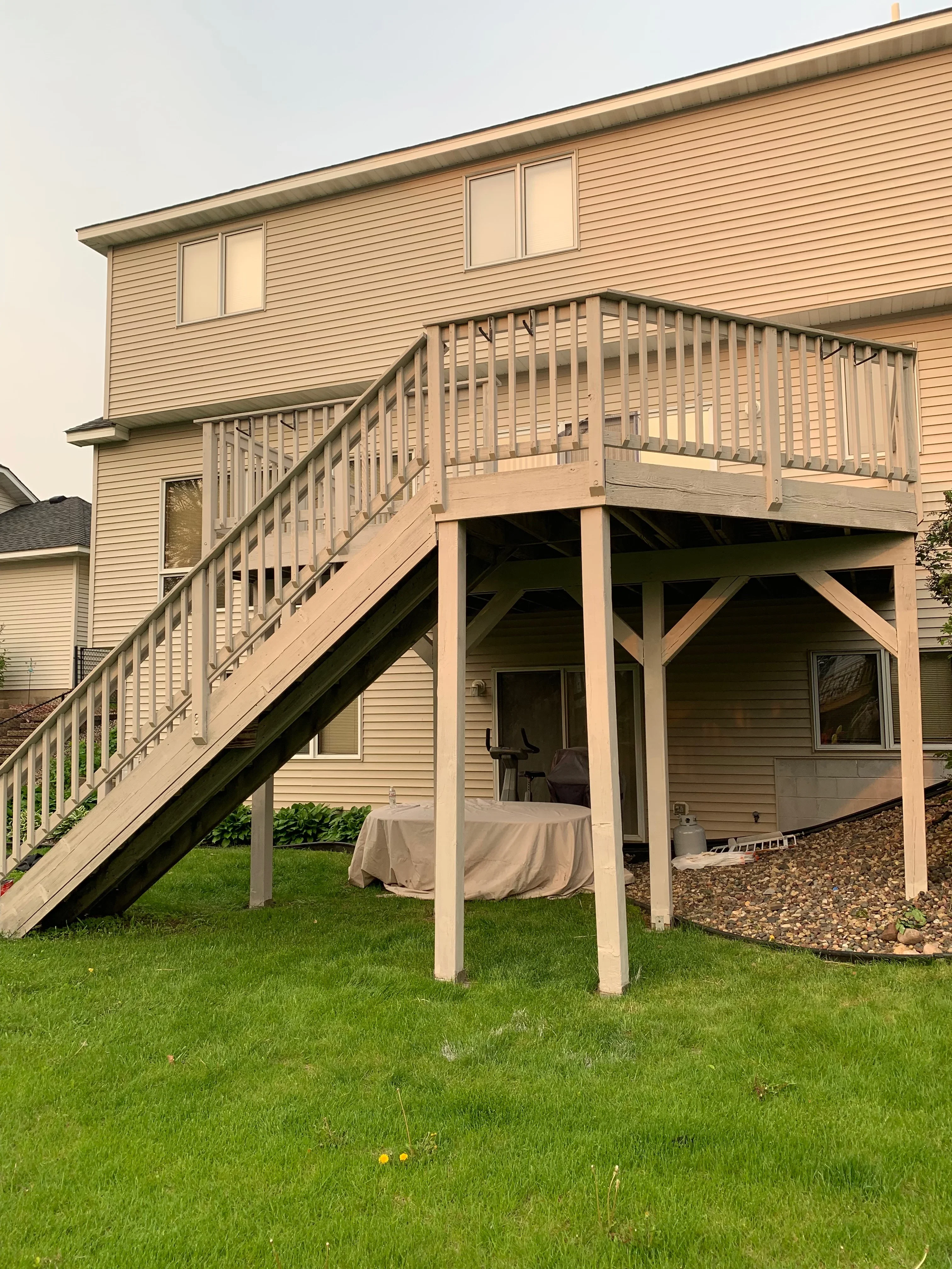 Two-level composite deck with stairs, railings, and covered patio structure attached to house