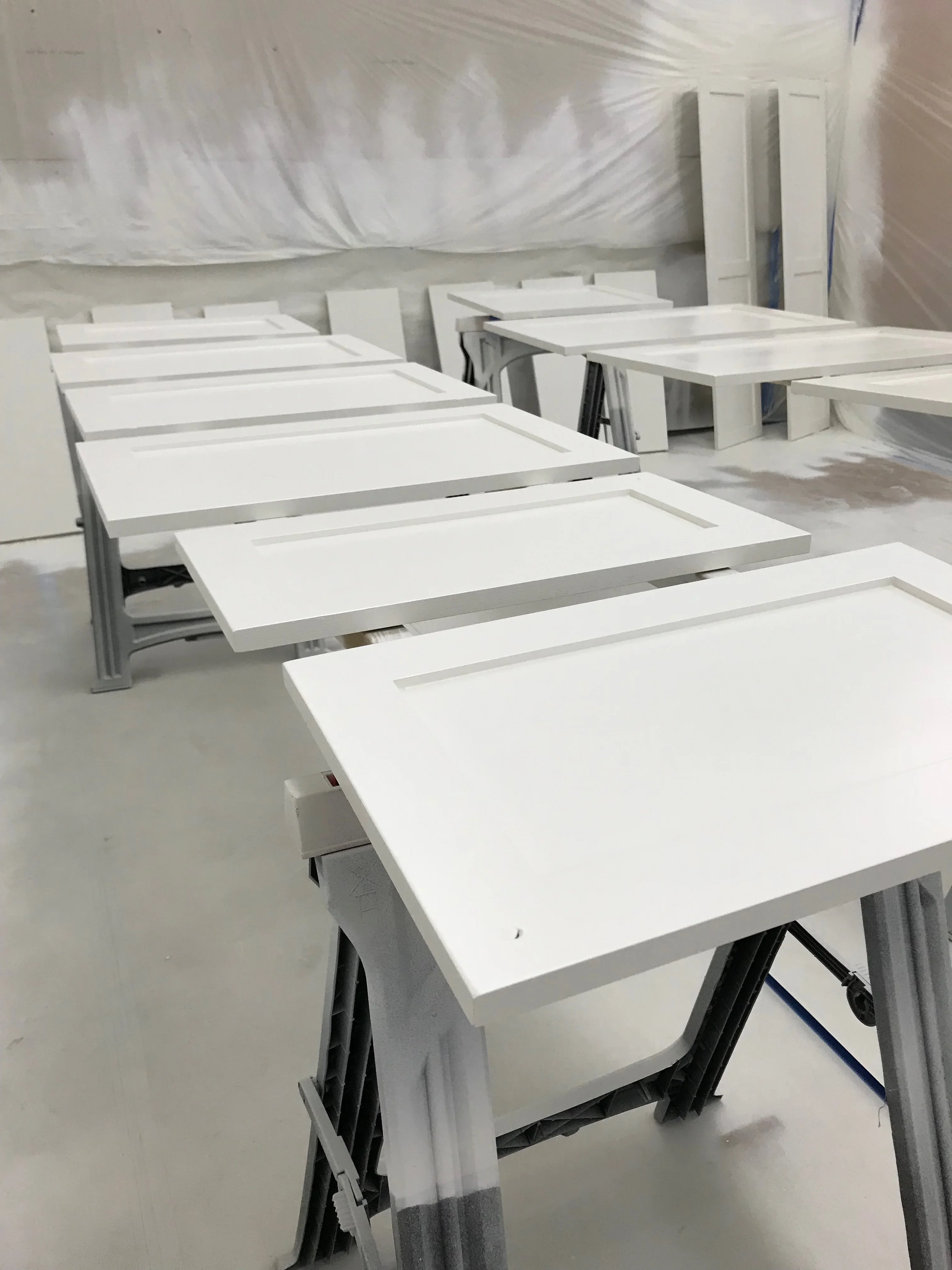 White painted cabinet doors and frames with protective coverings in finishing workshop