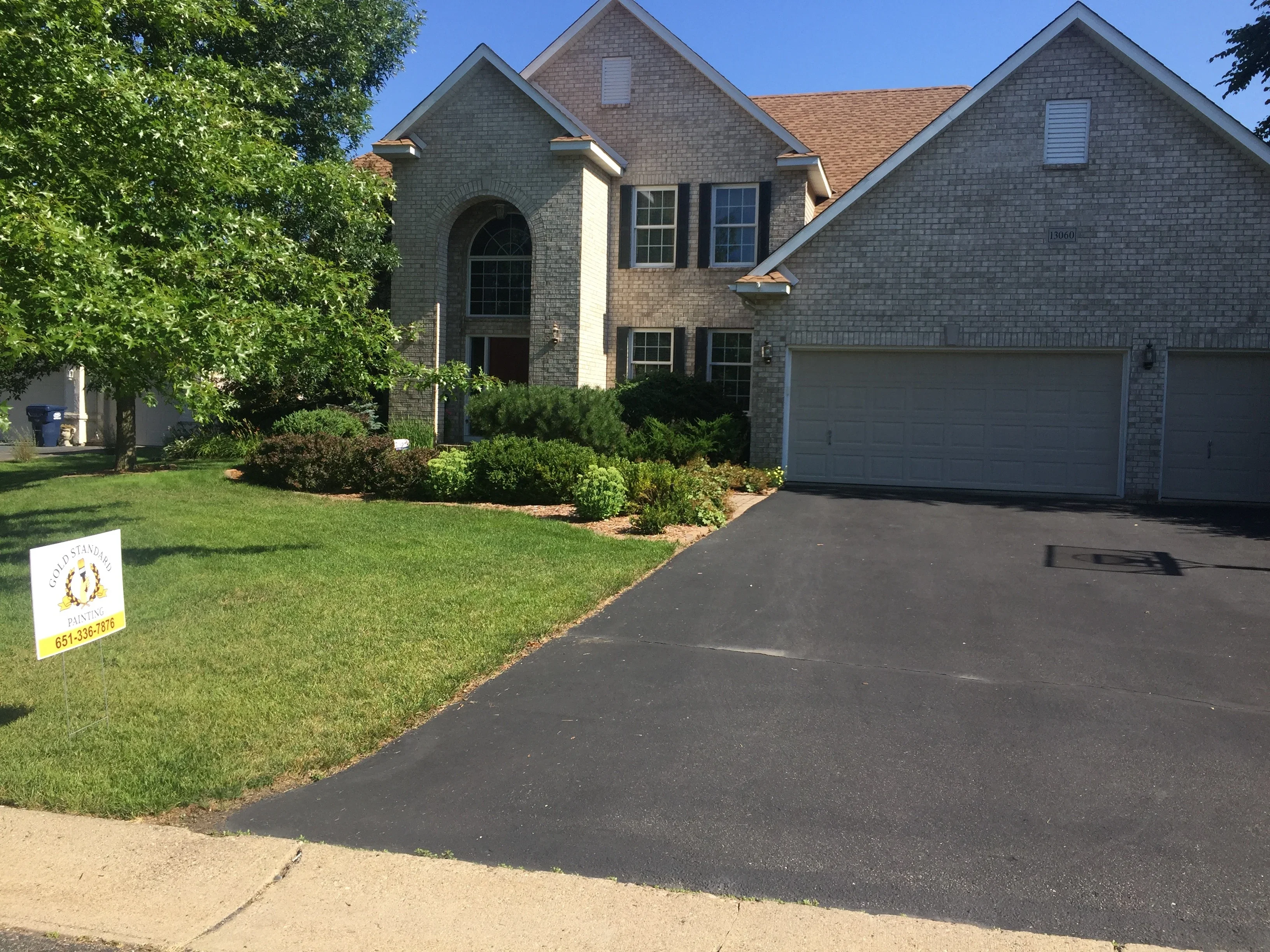 Newly sealed asphalt driveway with sharp edges and dark finish in front of brick home
