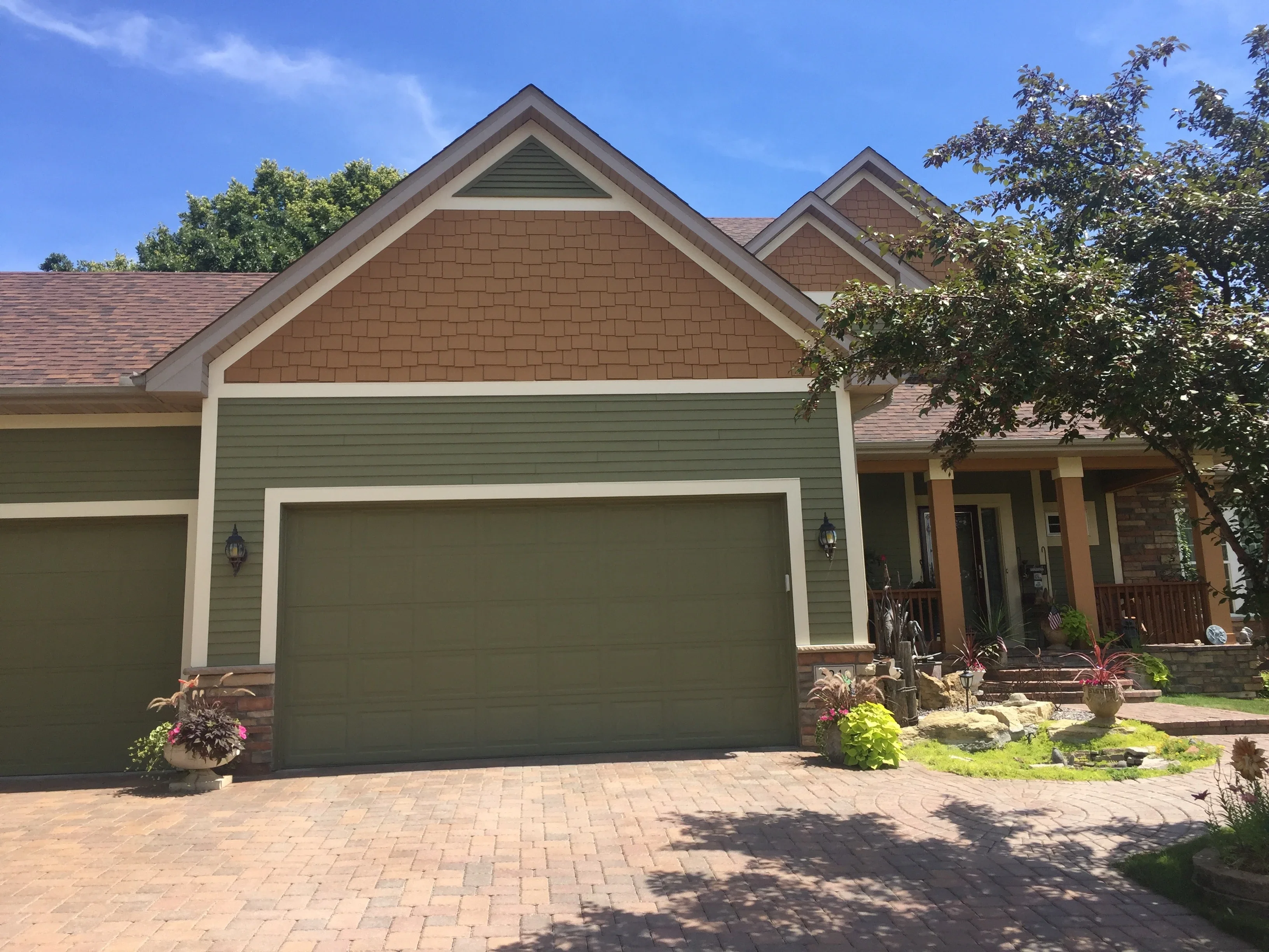 Sage green siding with white trim, brown cedar shake gable, and painted garage doors on residential home