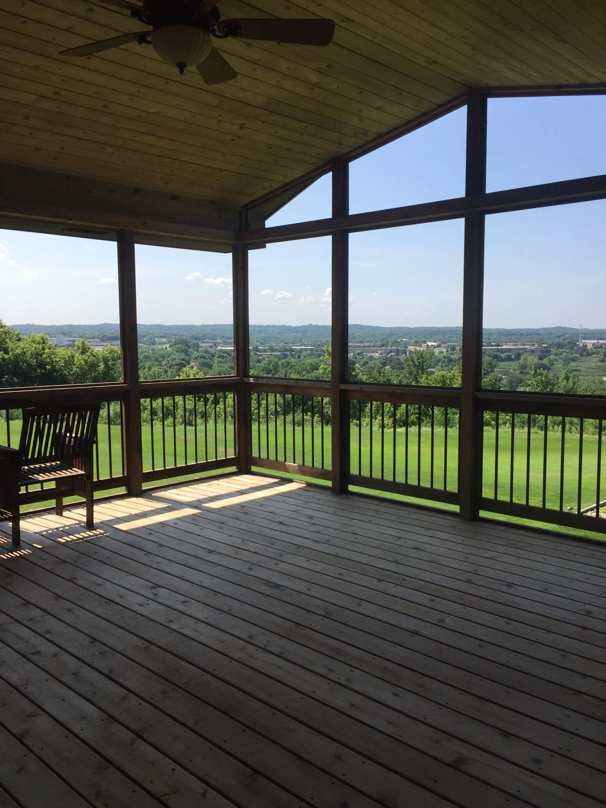 Screened porch with painted wood ceiling, stained deck, black frame screens, and metal railings