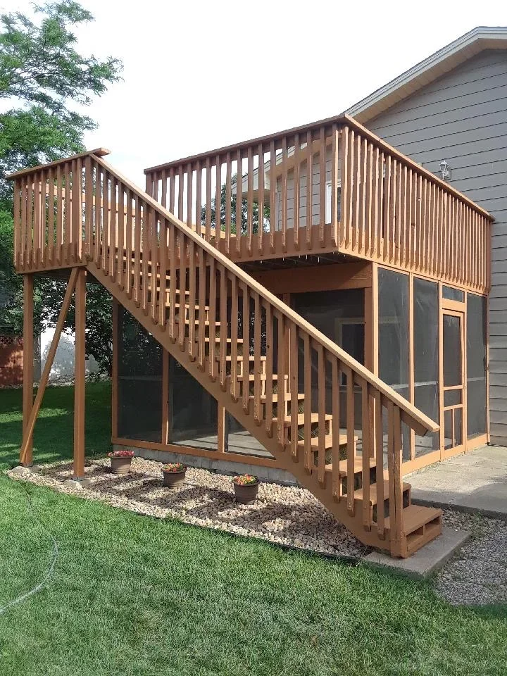 Two-level wooden deck with stained railings, vertical balusters, and connecting stairs attached to house