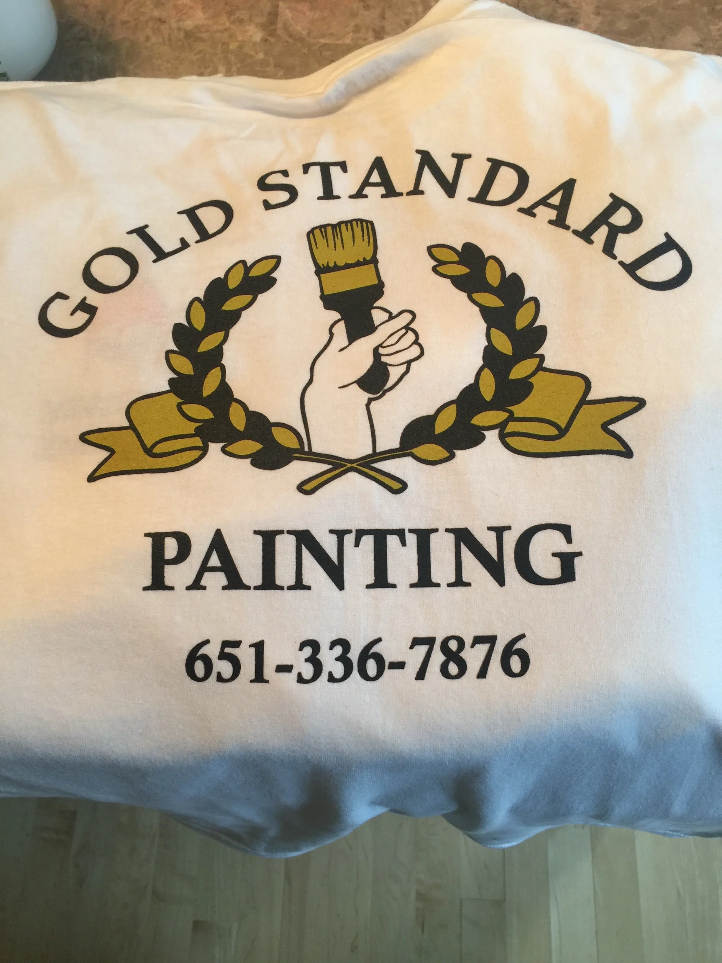 Screen-printed canvas apron with paintbrush logo and laurel wreath design in black and gold