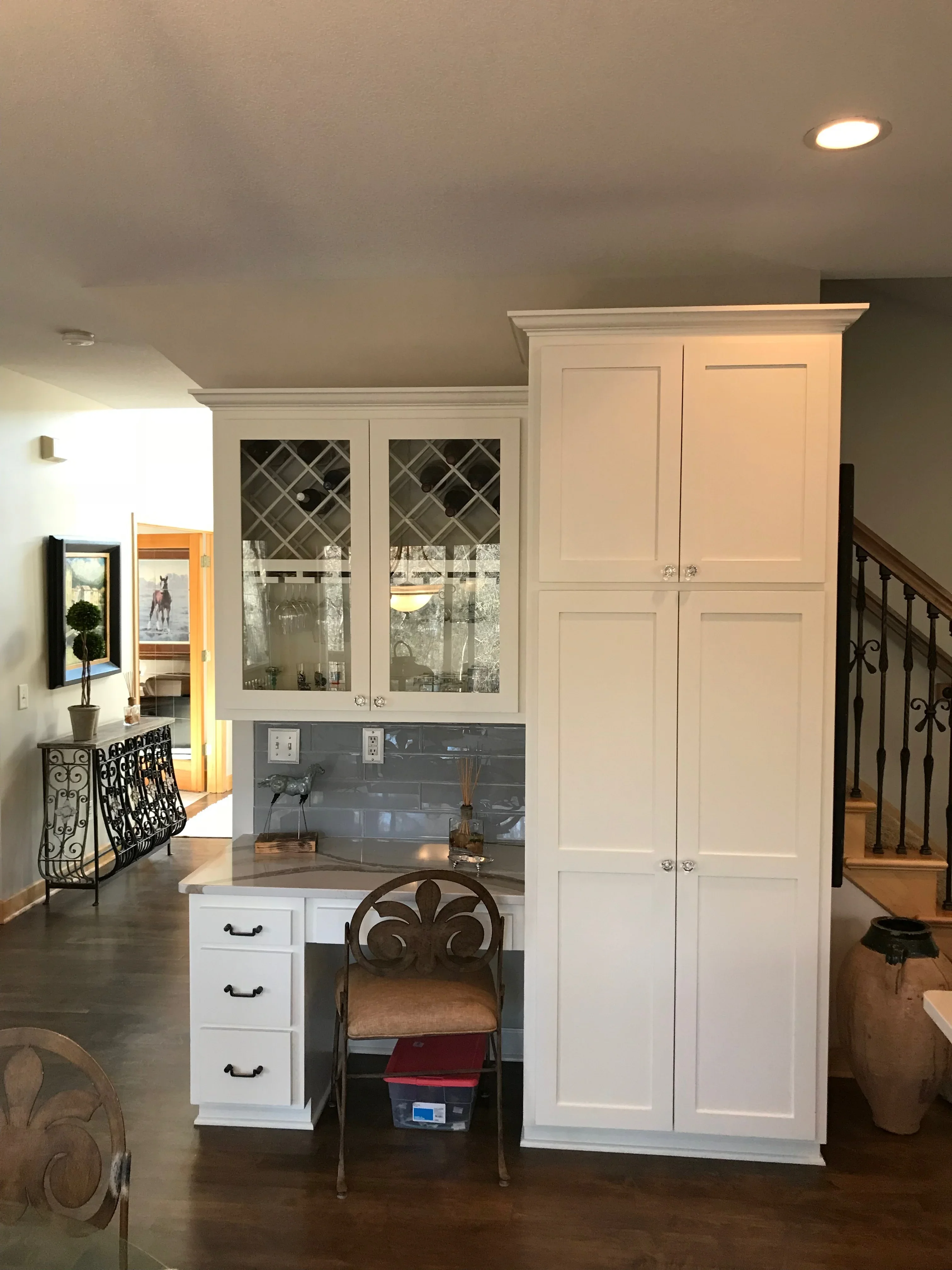 White painted built-in cabinetry with glass doors, gray tile backsplash, and integrated desk workspace