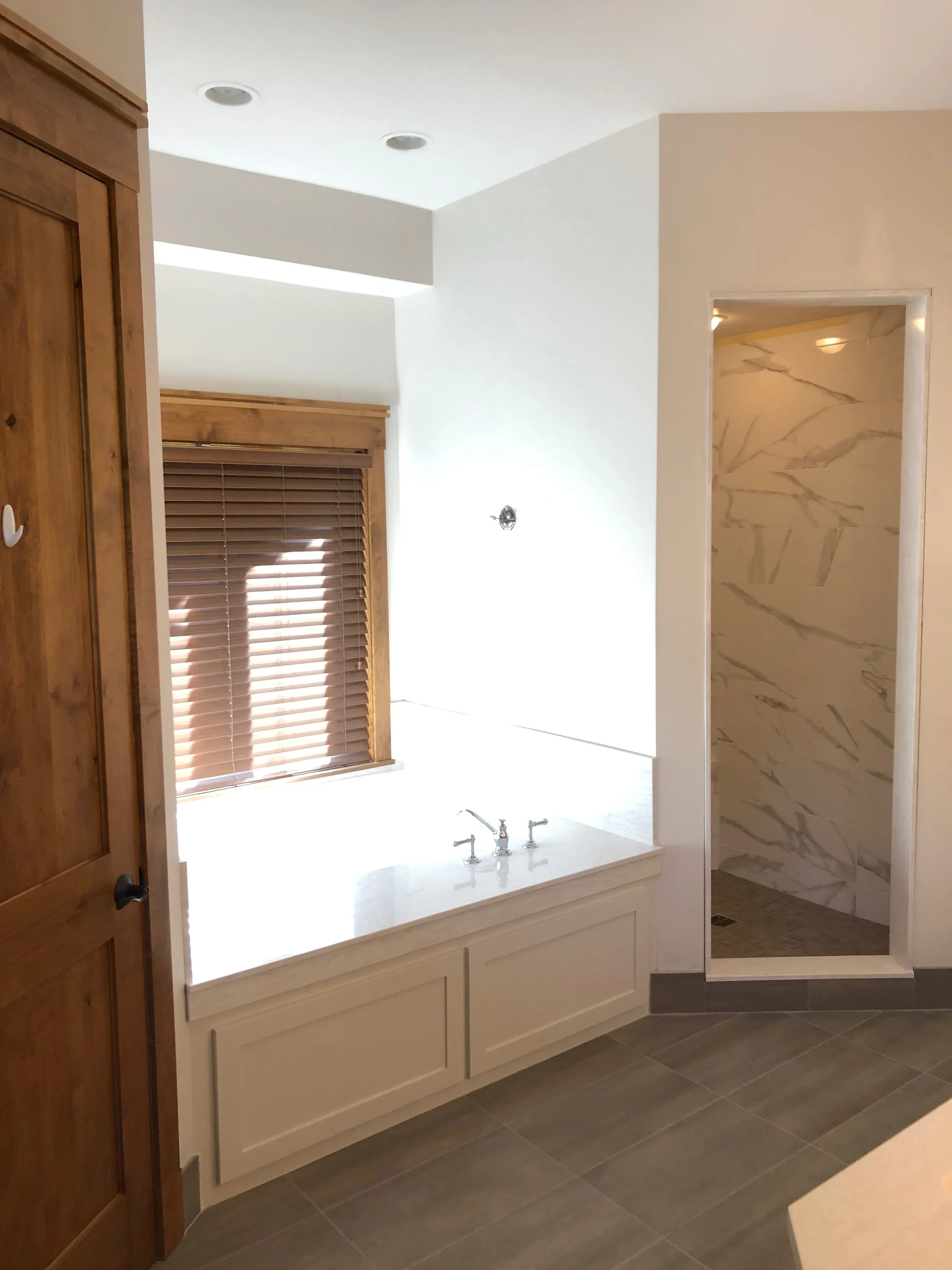 Painted bathroom with white walls, custom millwork tub surround, and marble tile shower