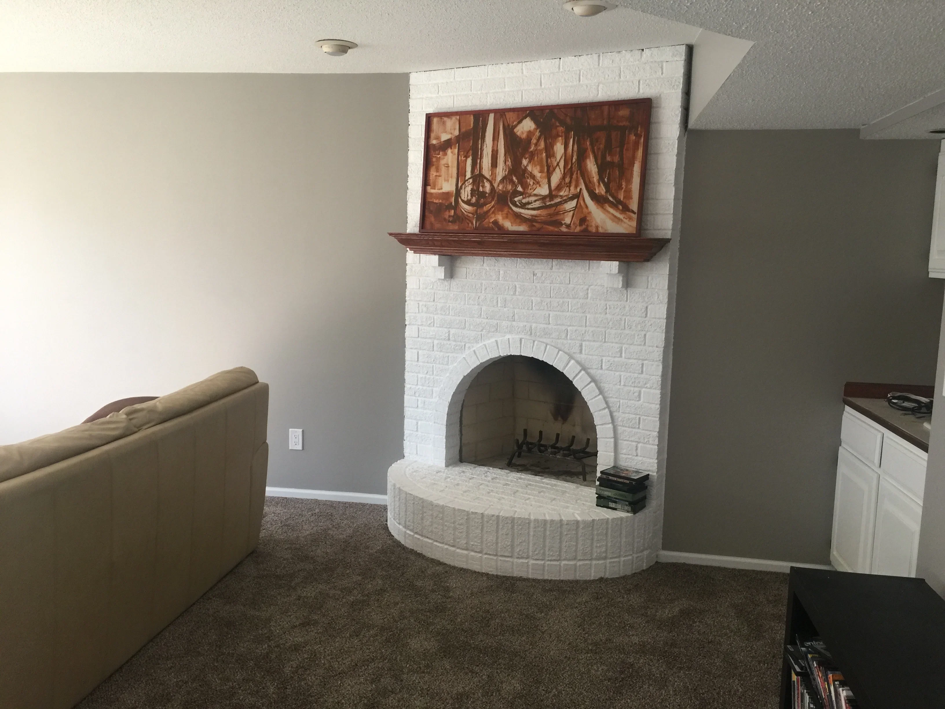 White painted brick fireplace with arched opening and gray-green accent wall in basement living area