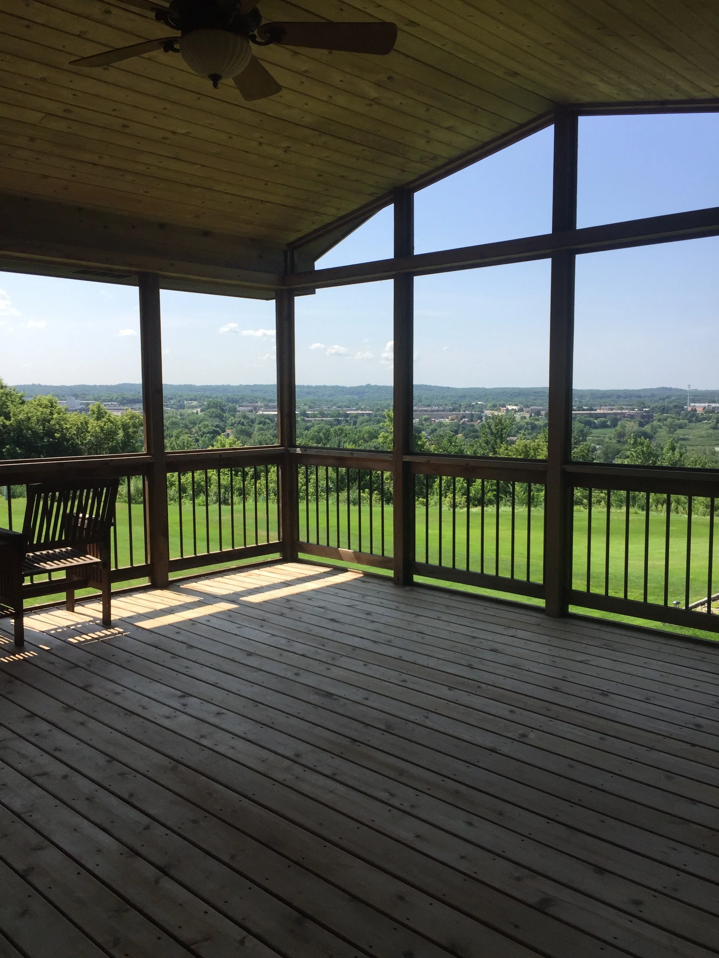 Screened porch interior with wood plank ceiling, dark wood railings, and composite deck flooring