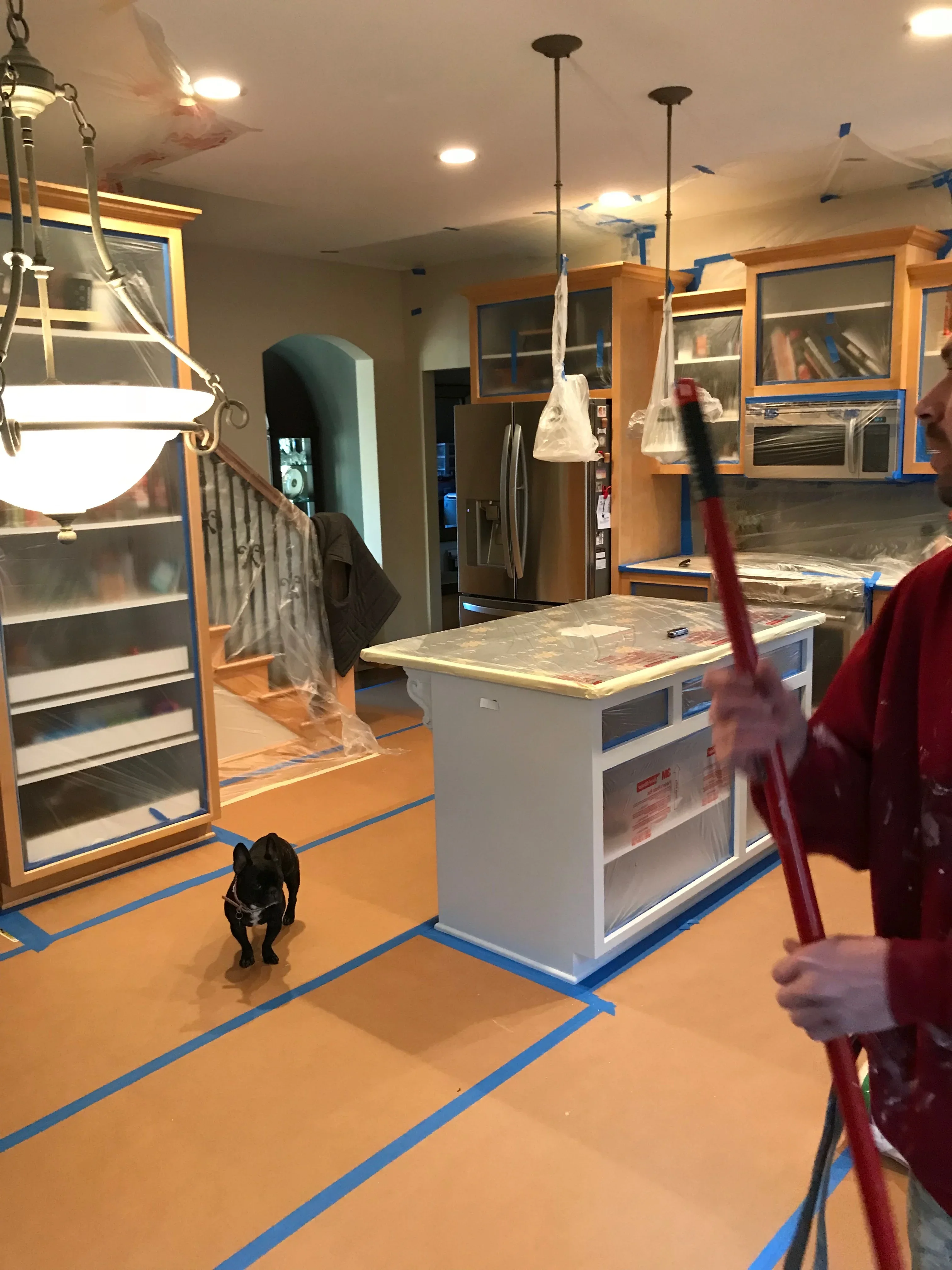 Kitchen interior with fresh paint, wood cabinetry, island, and protective masking during renovation